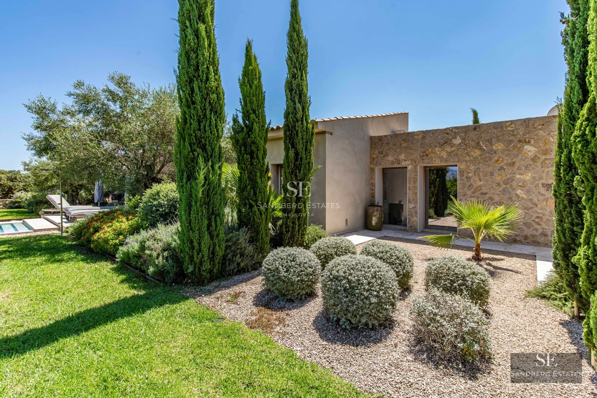 Aerial view of a luxurious house featuring an infinity pool, lush garden, and modern architecture with expansive windows.