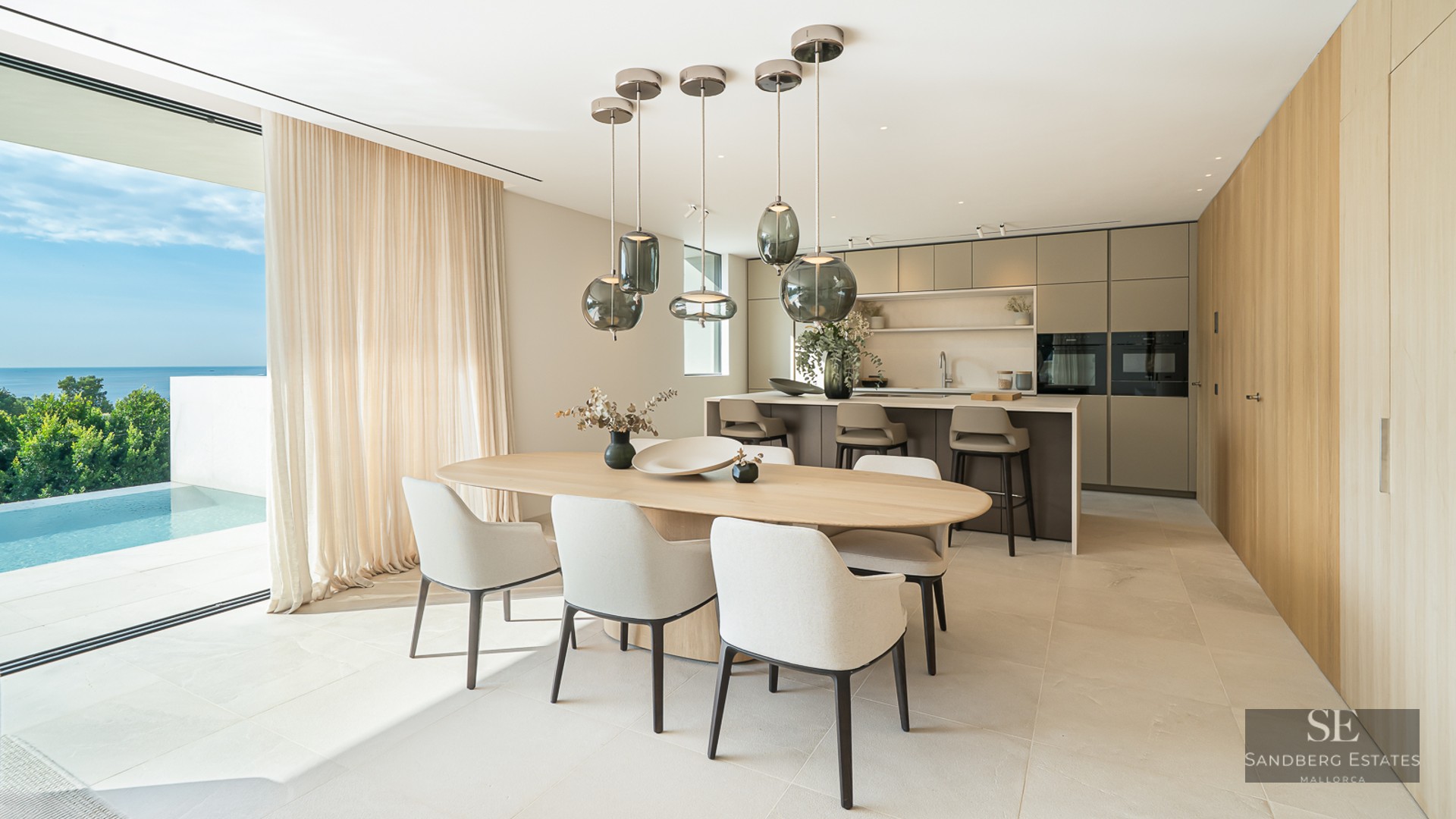 Contemporary dining room with wooden table and glass pendant lights, overlooking an infinity pool and the sea.