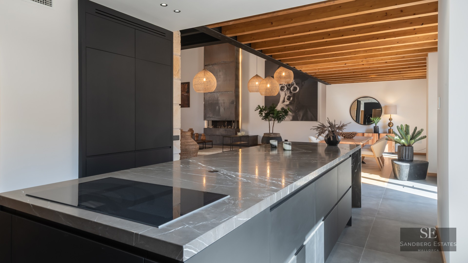 Modern kitchen featuring a large grey marble island, matte black cabinets, and exposed wooden ceiling beams.