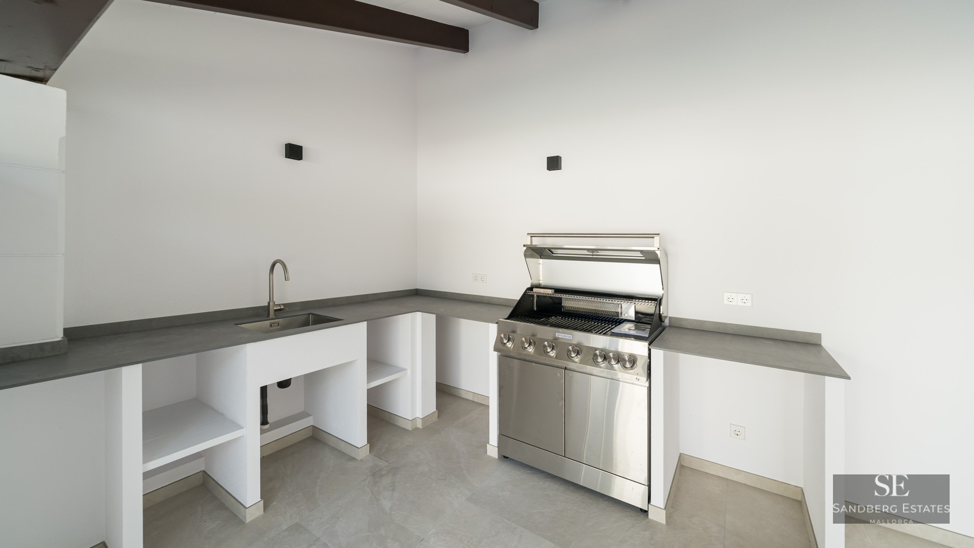 Contemporary outdoor kitchen featuring a stainless steel grill, integrated sink, and sleek gray countertops.