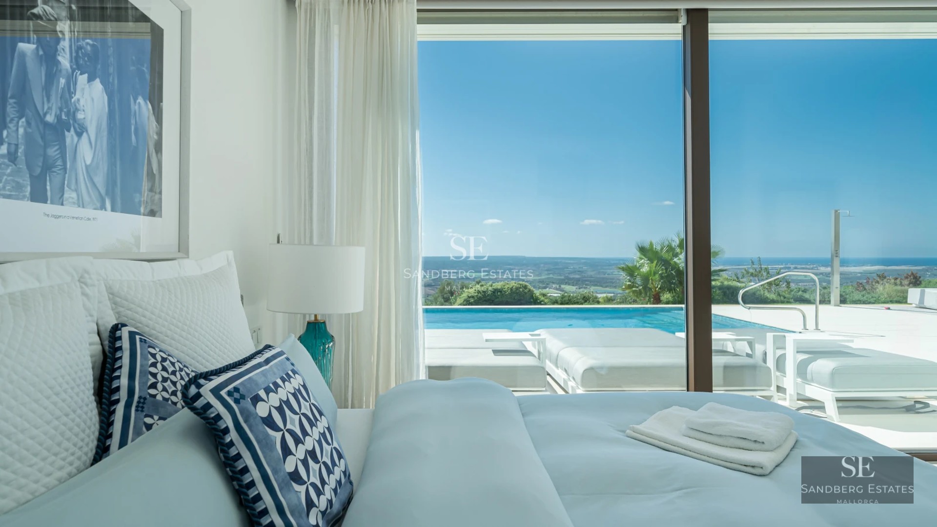 View of a modern pool surrounded by lush greenery and a house with large windows and minimalist design.