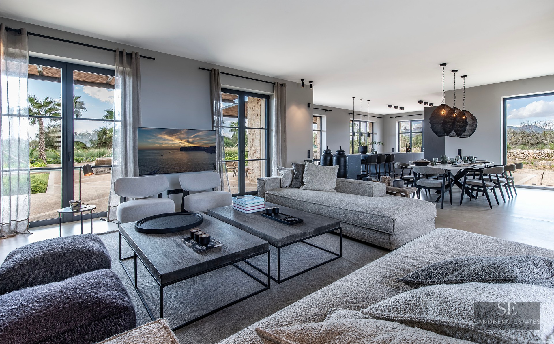 Spacious modern living room with grey sofas, wooden coffee tables, and dining area looking out to a garden.