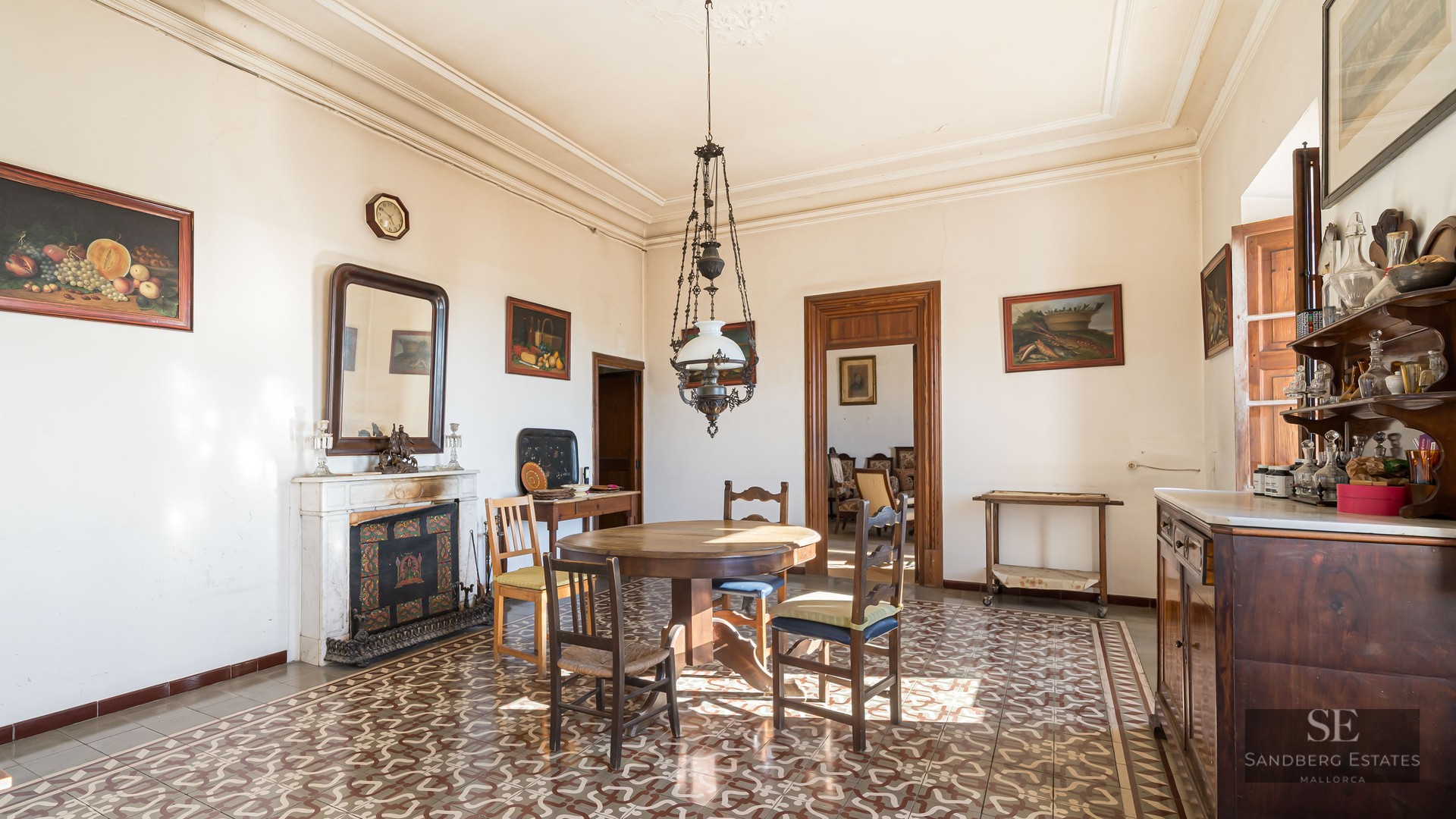 Antique dining room with wooden table, ornate floor tiles, marble fireplace, and high ceilings.