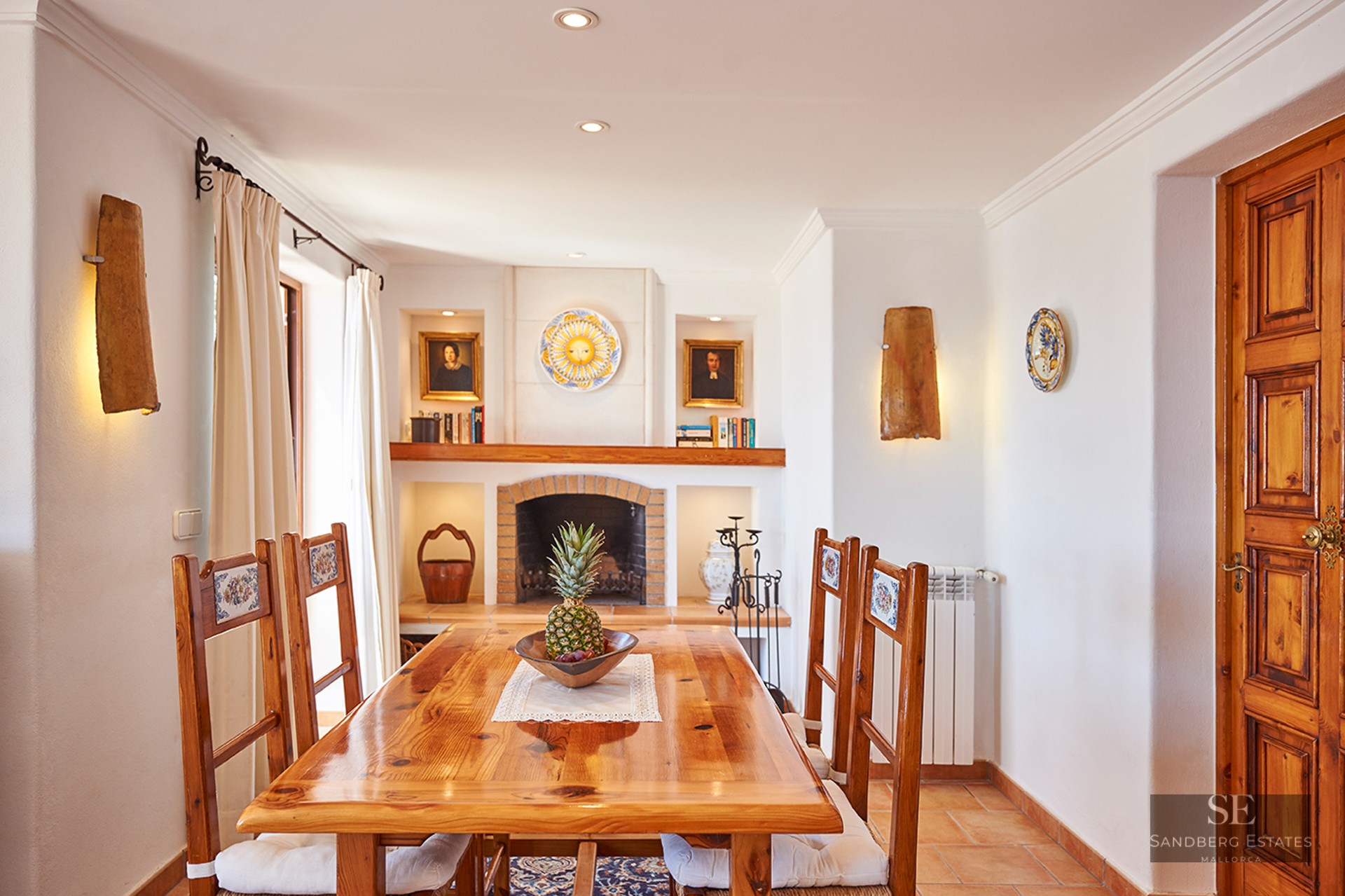 A wooden dining table and chairs in front of a brick fireplace in a Mediterranean-style room.