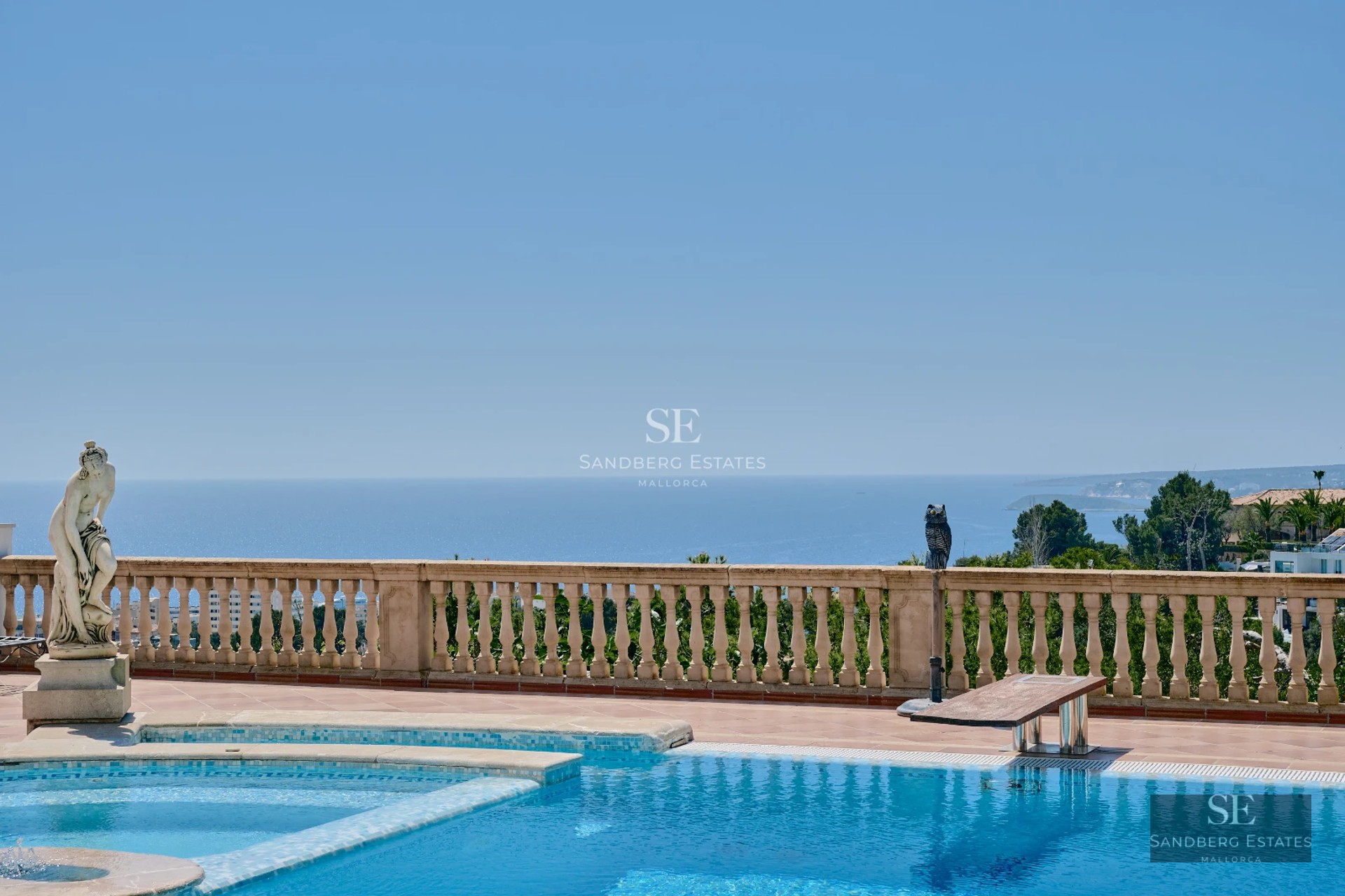 Panoramic view of an infinity pool with sun loungers, surrounded by greenery and modern, minimalist architecture.