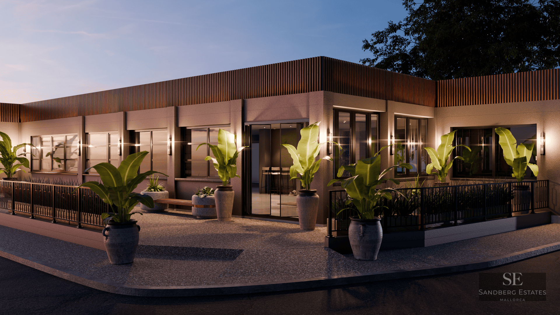 Bâtiment moderne d'un étage au crépuscule avec des lattes de bois, de grandes fenêtres et des plantes tropicales en pot.