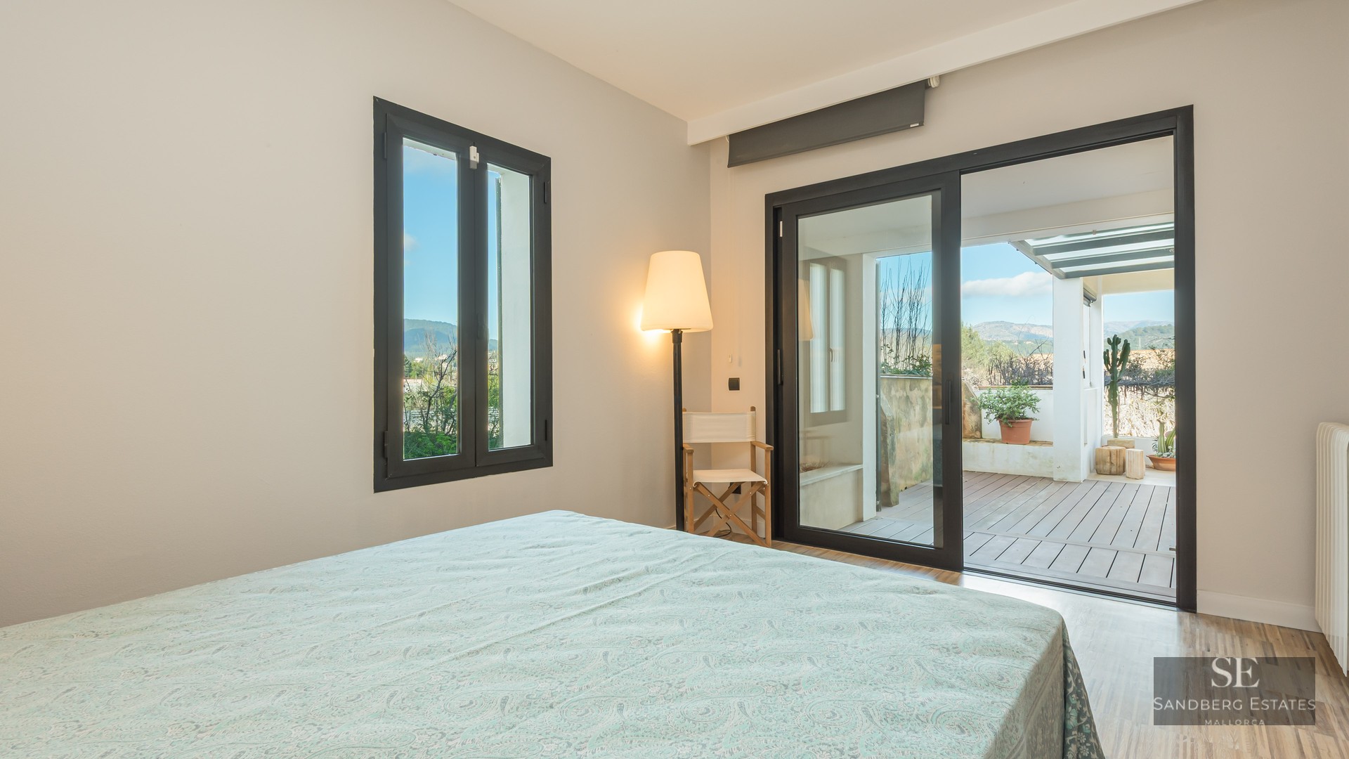 Bright bedroom with sliding glass doors opening to a wood-decked terrace with mountain views.
