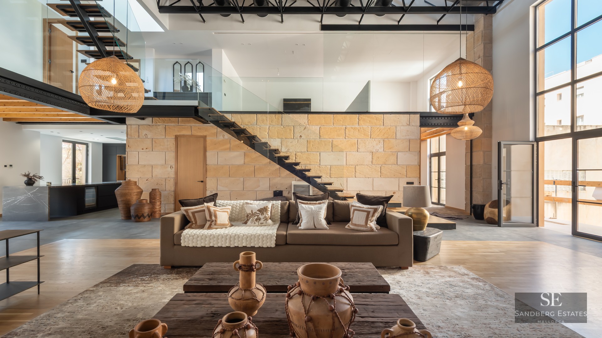 Modern living room featuring a stone wall, floating staircase, large wicker lamps, and a comfortable brown sofa.
