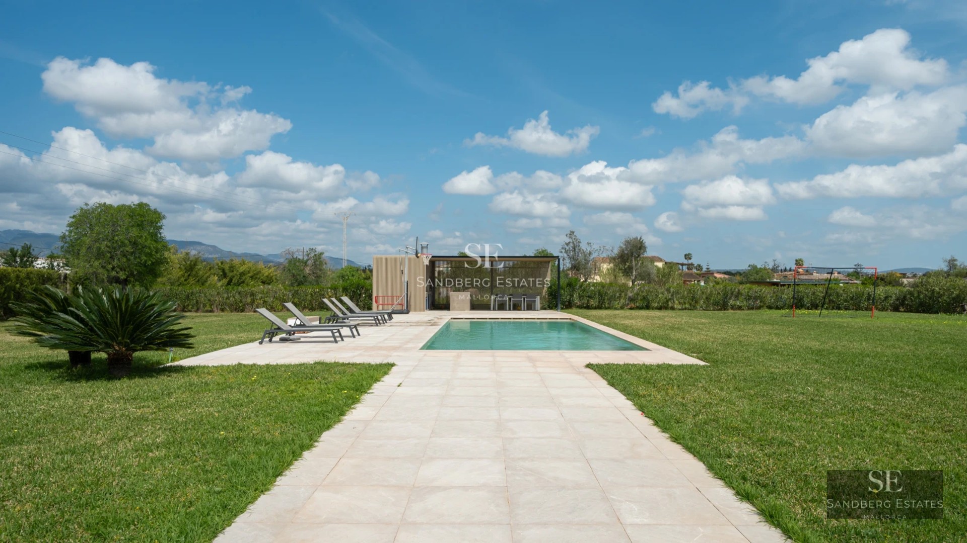 Spacious balcony with sea view, modern outdoor furniture, glass railing, wood flooring, and lush vegetation.