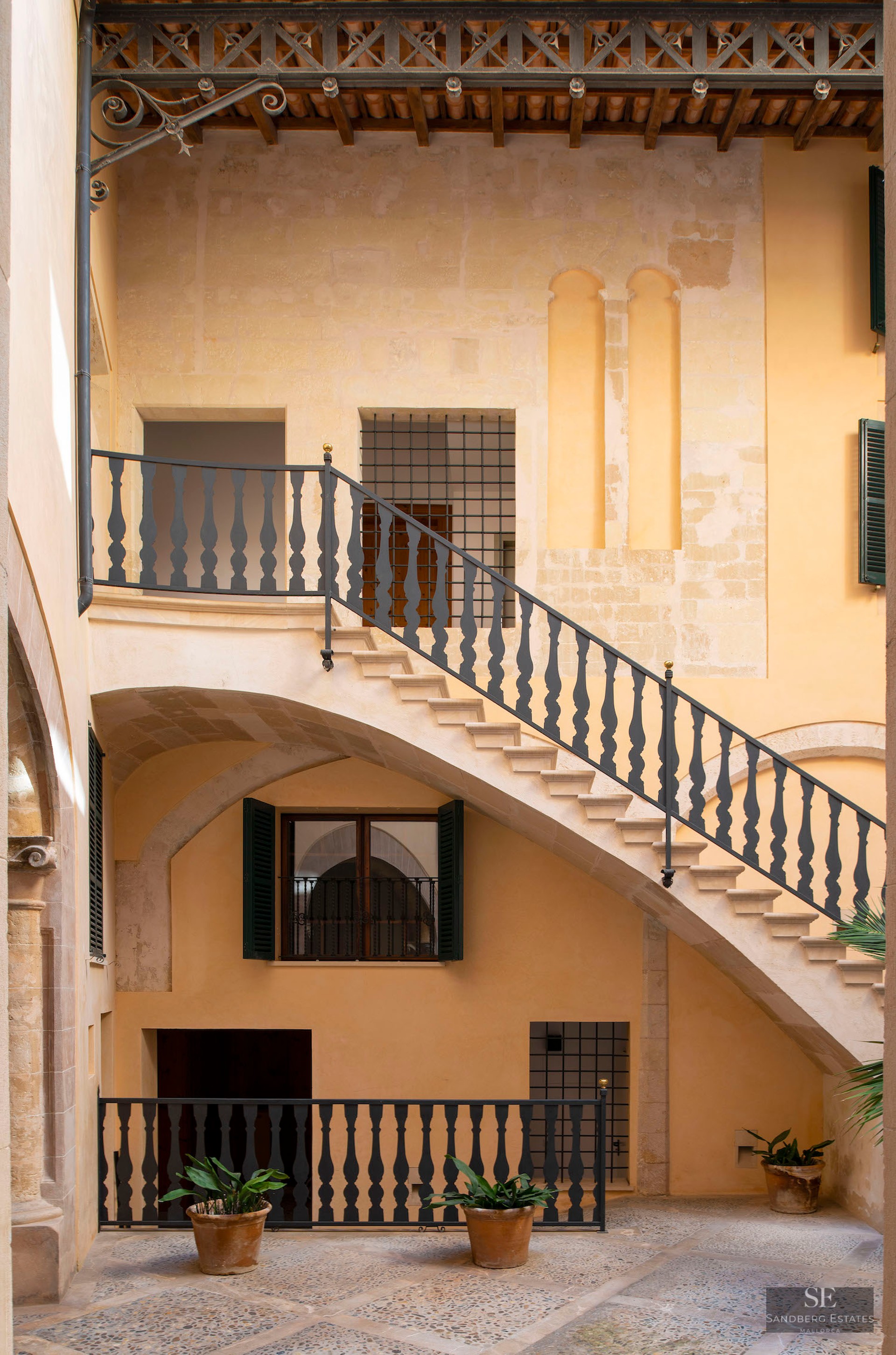 View of an inner courtyard with a stone staircase, black wrought iron railings, and warm ochre stone walls.