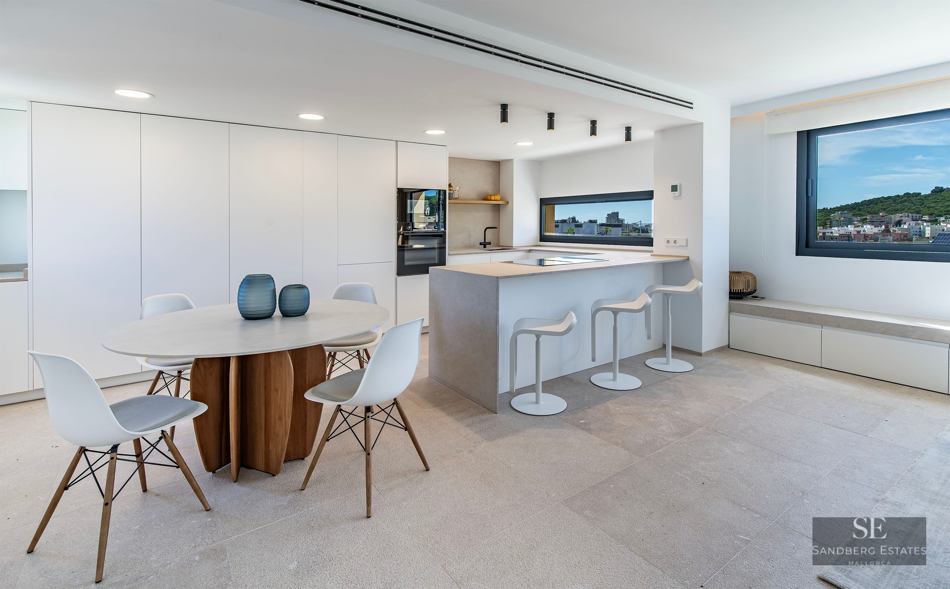 Modern kitchen with stone island, breakfast bar, and round dining table near a window with a city view.