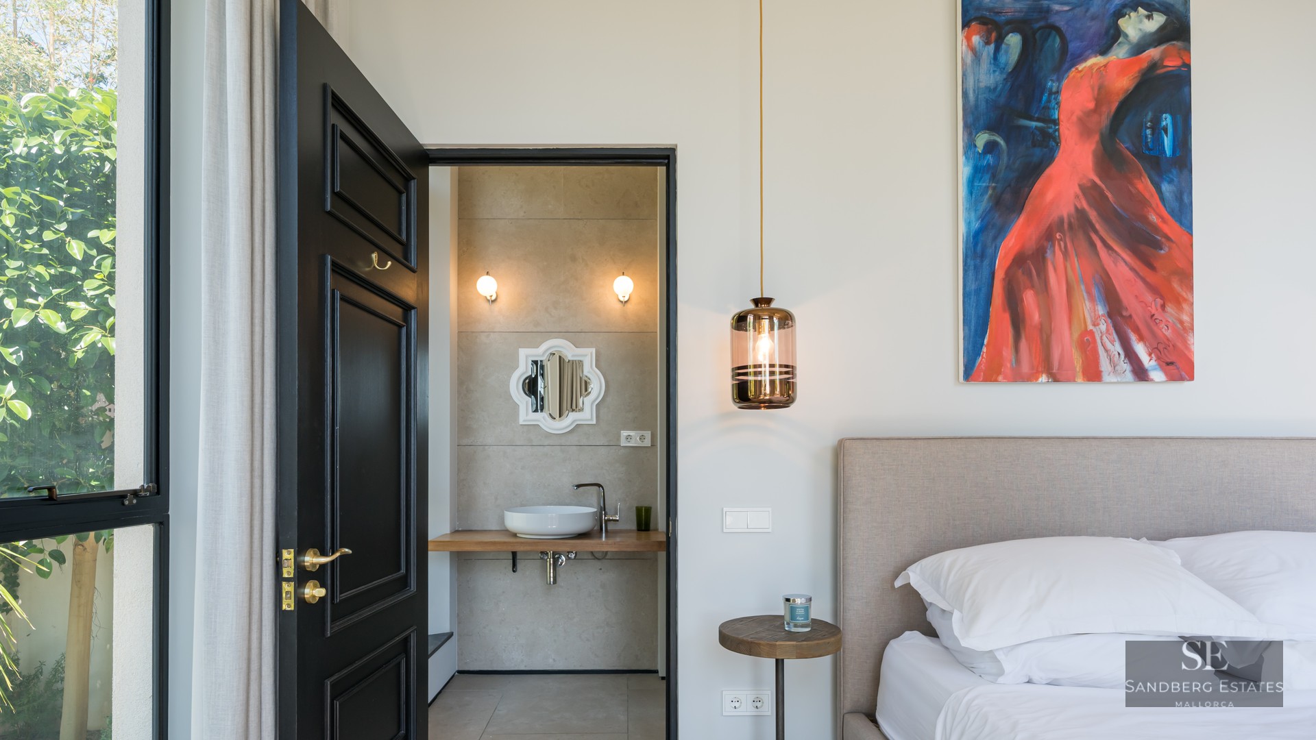 Luxury bedroom with black door leading to a modern ensuite bathroom, featuring a large painting and pendant light.
