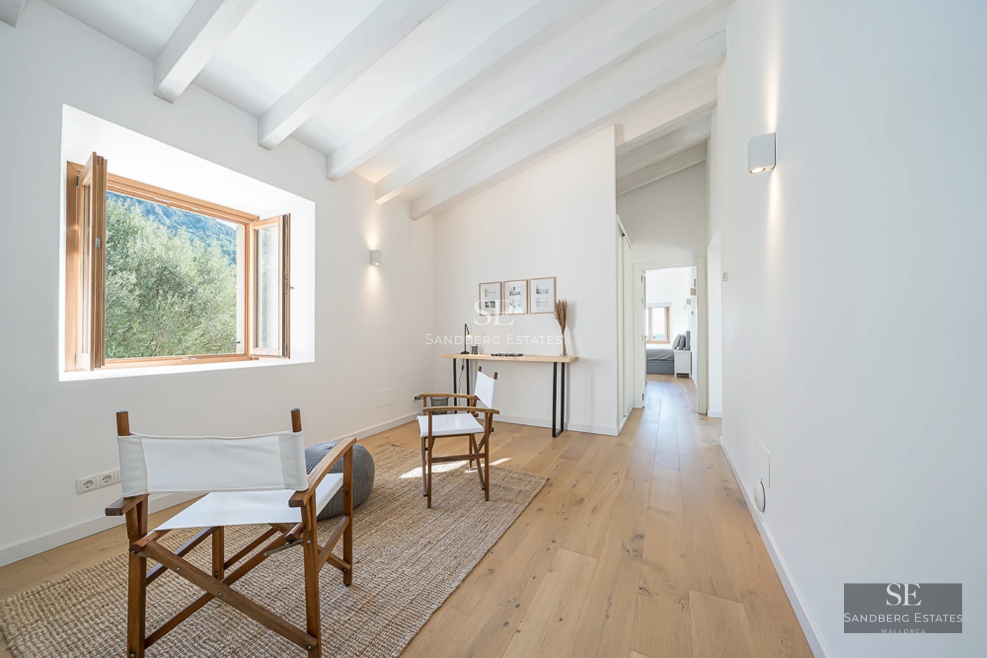 Spacious living room with large windows, light wood floor, grey modular sofa, and view of lush garden. Modern and elegant design.