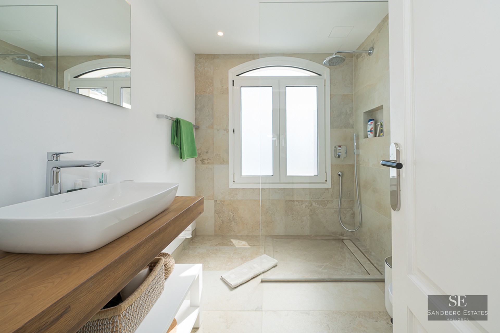 Salle de bain lumineuse avec vasque sur plan en bois et douche en pierre avec fenêtre cintrée.