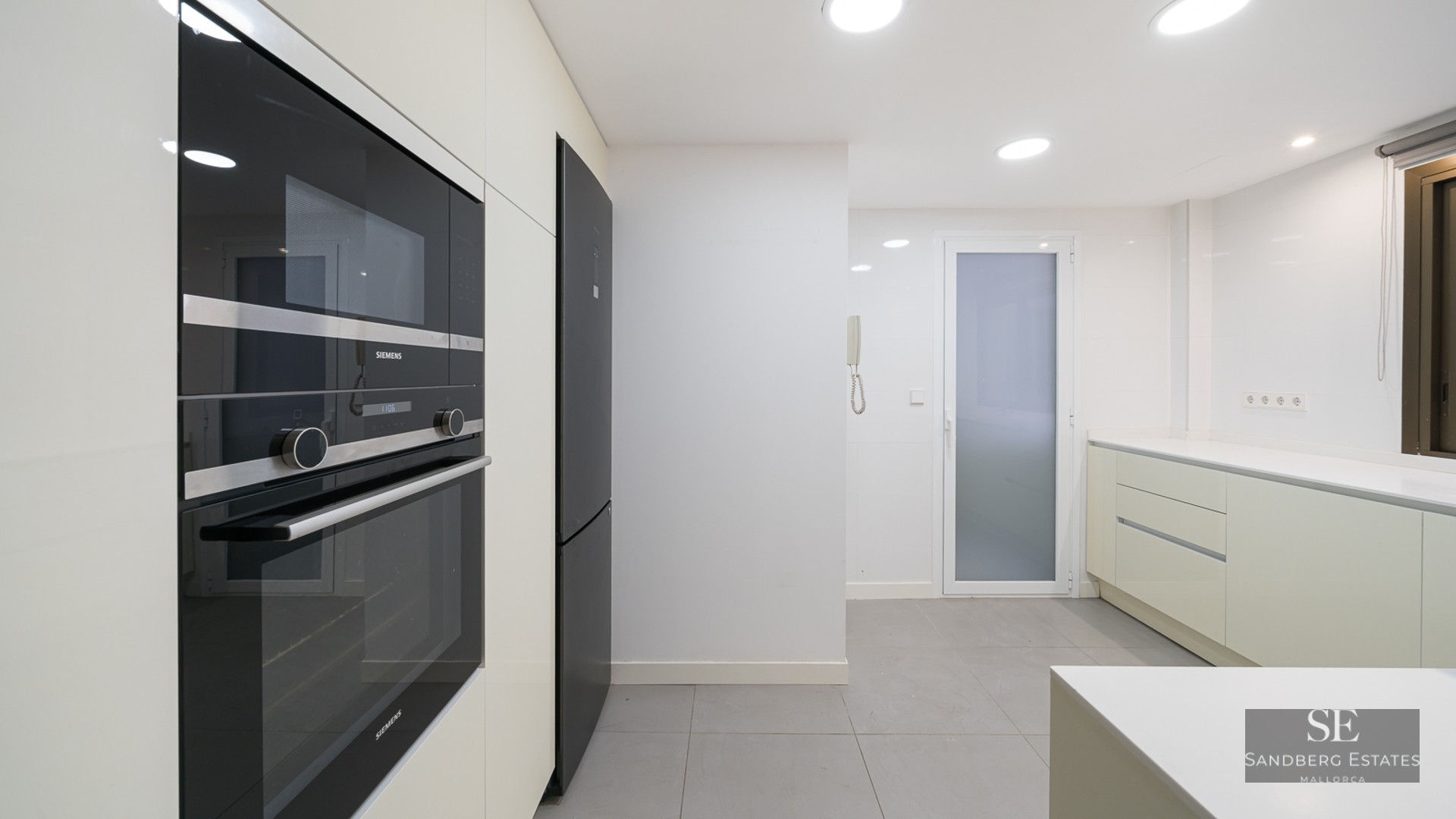 Modern white kitchen with built-in black Siemens oven and microwave, grey floor tiles, and recessed lighting.
