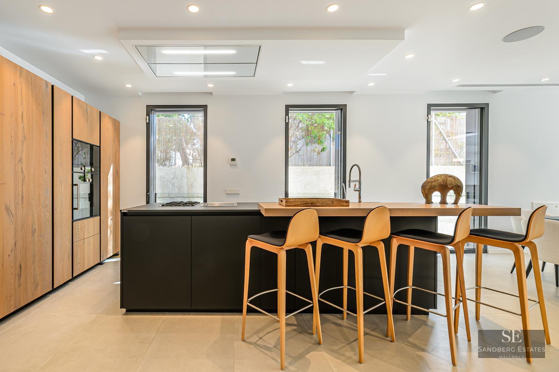 Modern kitchen featuring a black island with wooden breakfast bar, four stools, and floor-to-ceiling wooden cabinets.