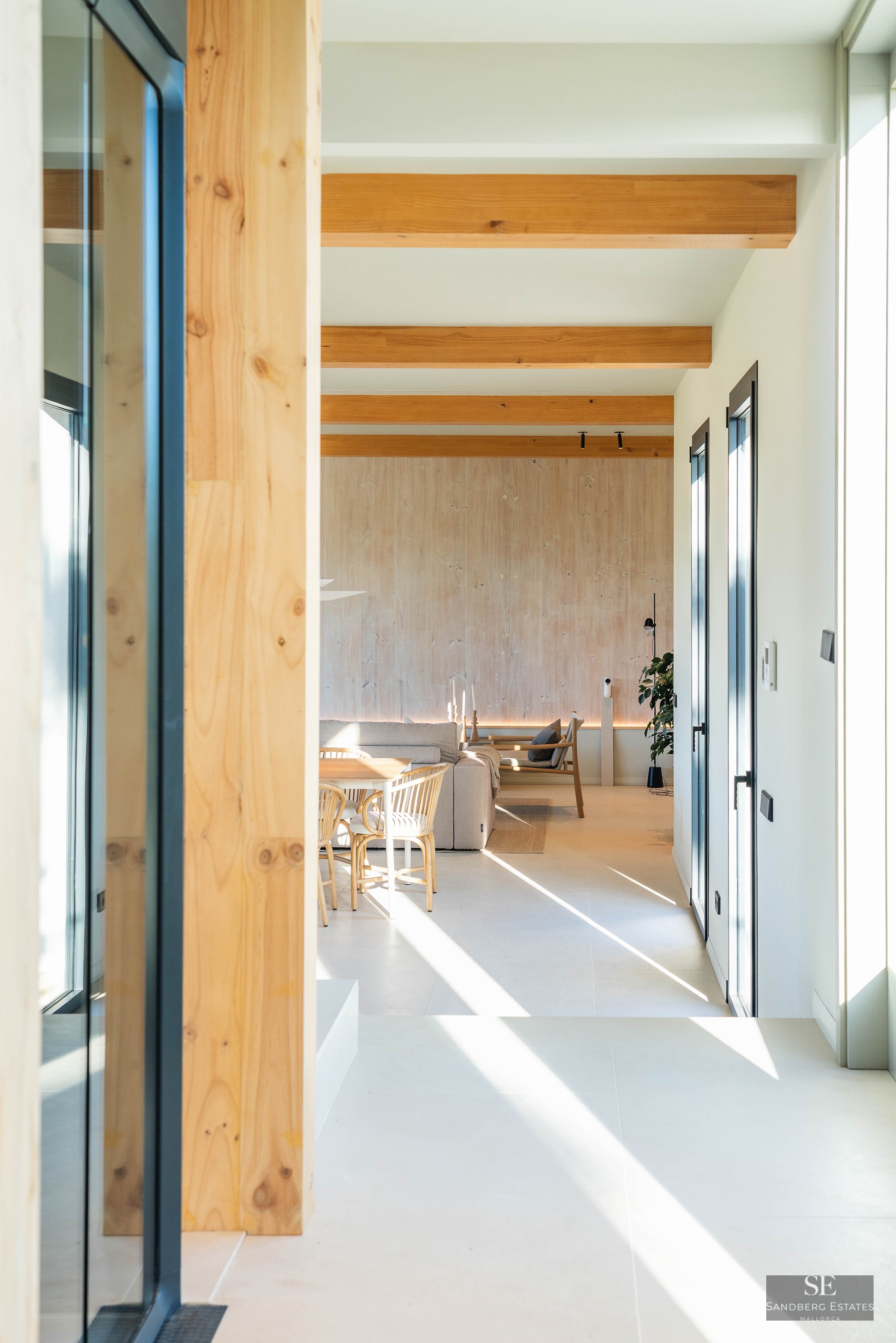 Modern living room featuring exposed wooden beams, beige sofa, and strong sunlight through large windows.