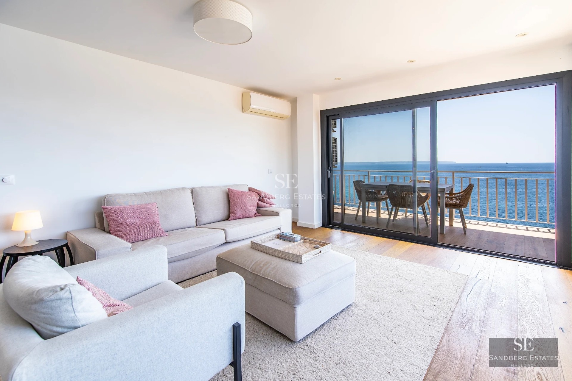 Bright modern interior with sea views. Balcony with glass railing, stylish furniture, and a pool visible outside.