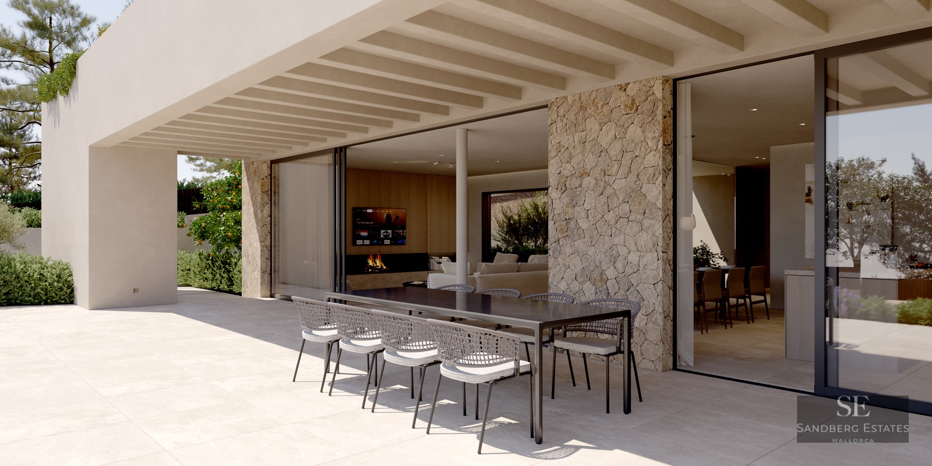 A modern covered terrace with a large black dining table, woven chairs, natural stone wall, and sliding glass doors.