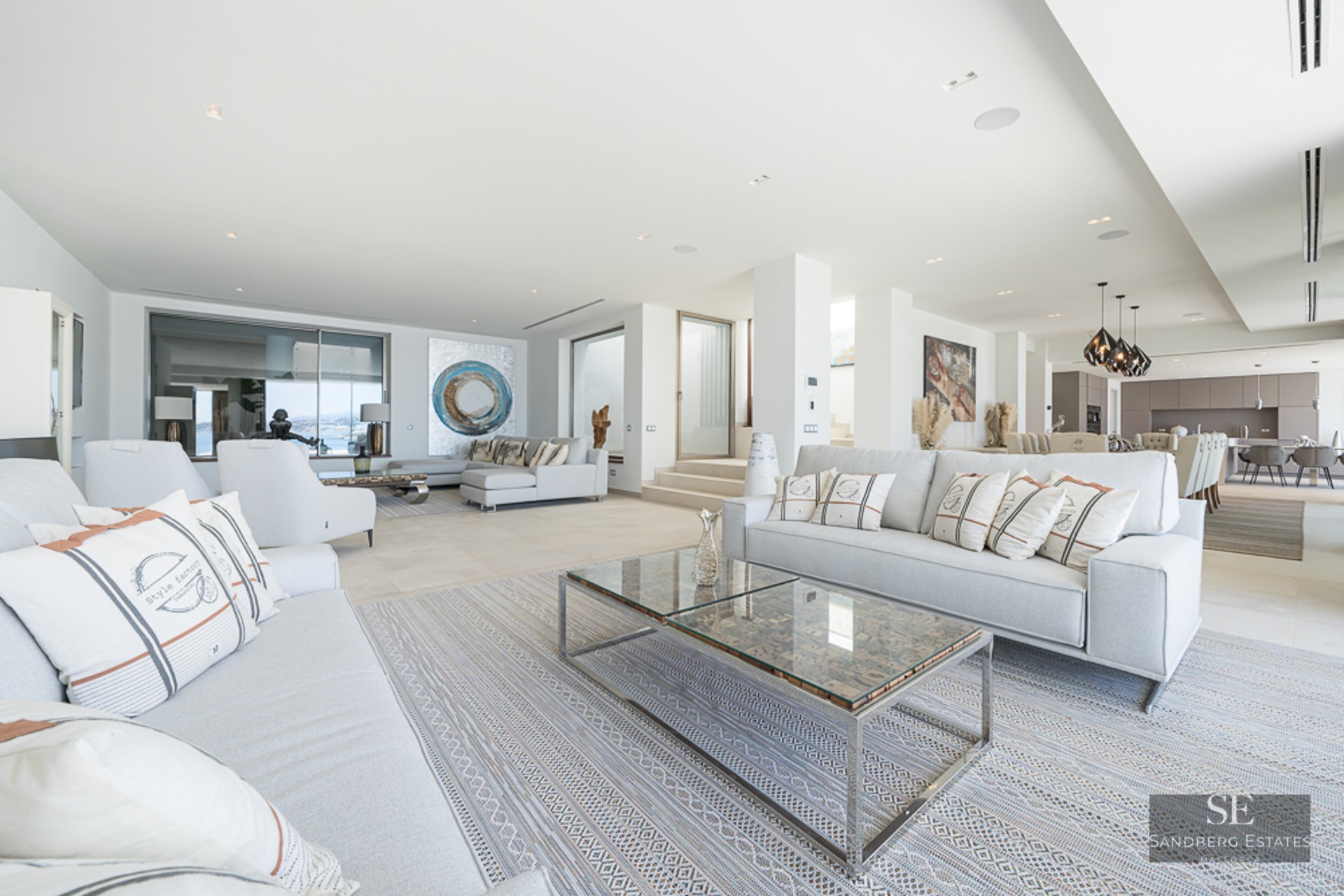 Spacious modern living room with grey sofas, glass coffee tables, and a view of the open-concept kitchen.