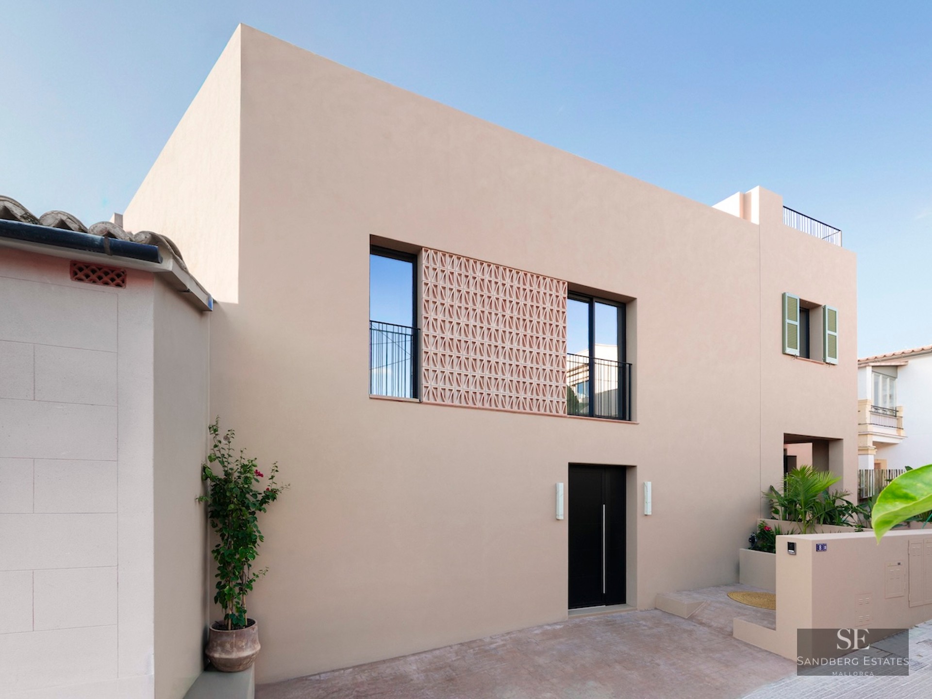 Façade beige avec porte noire, fenêtres à balustrades et écran décoratif en terre cuite.