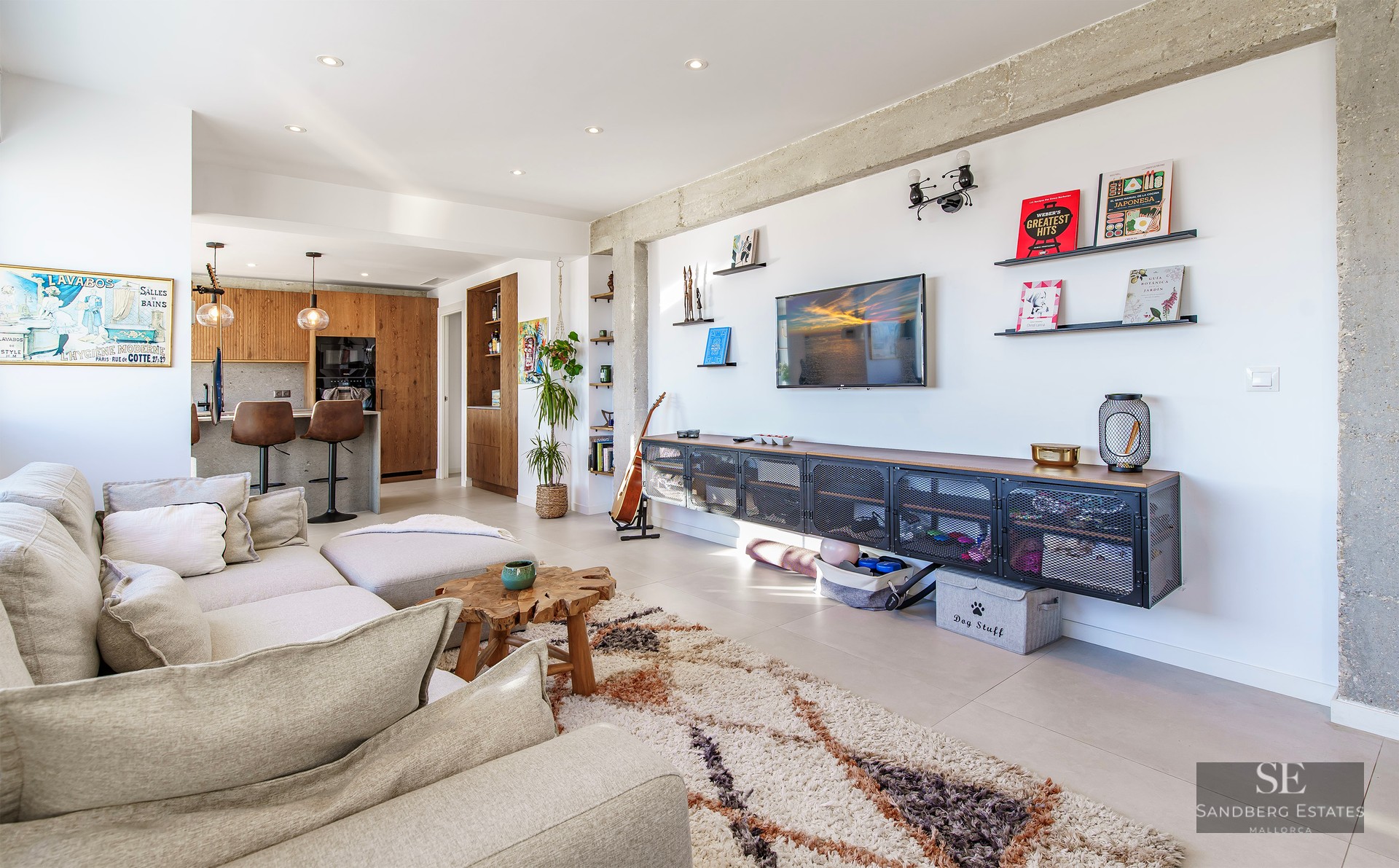 Spacious living room featuring a beige sectional sofa, shaggy rug, exposed concrete beams, and an open-plan kitchen.