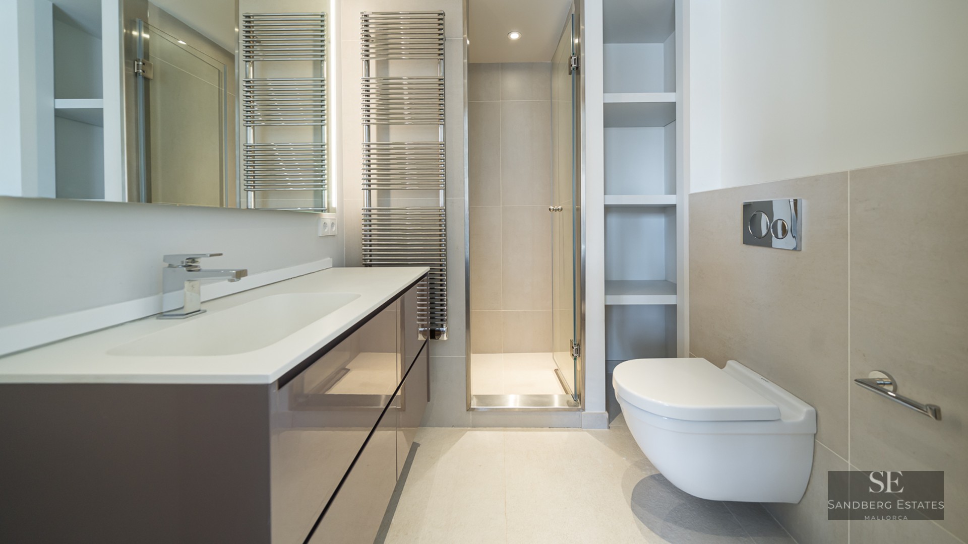 Modern bathroom with a large vanity, glass walk-in shower, wall-hung toilet, and chrome towel radiator.