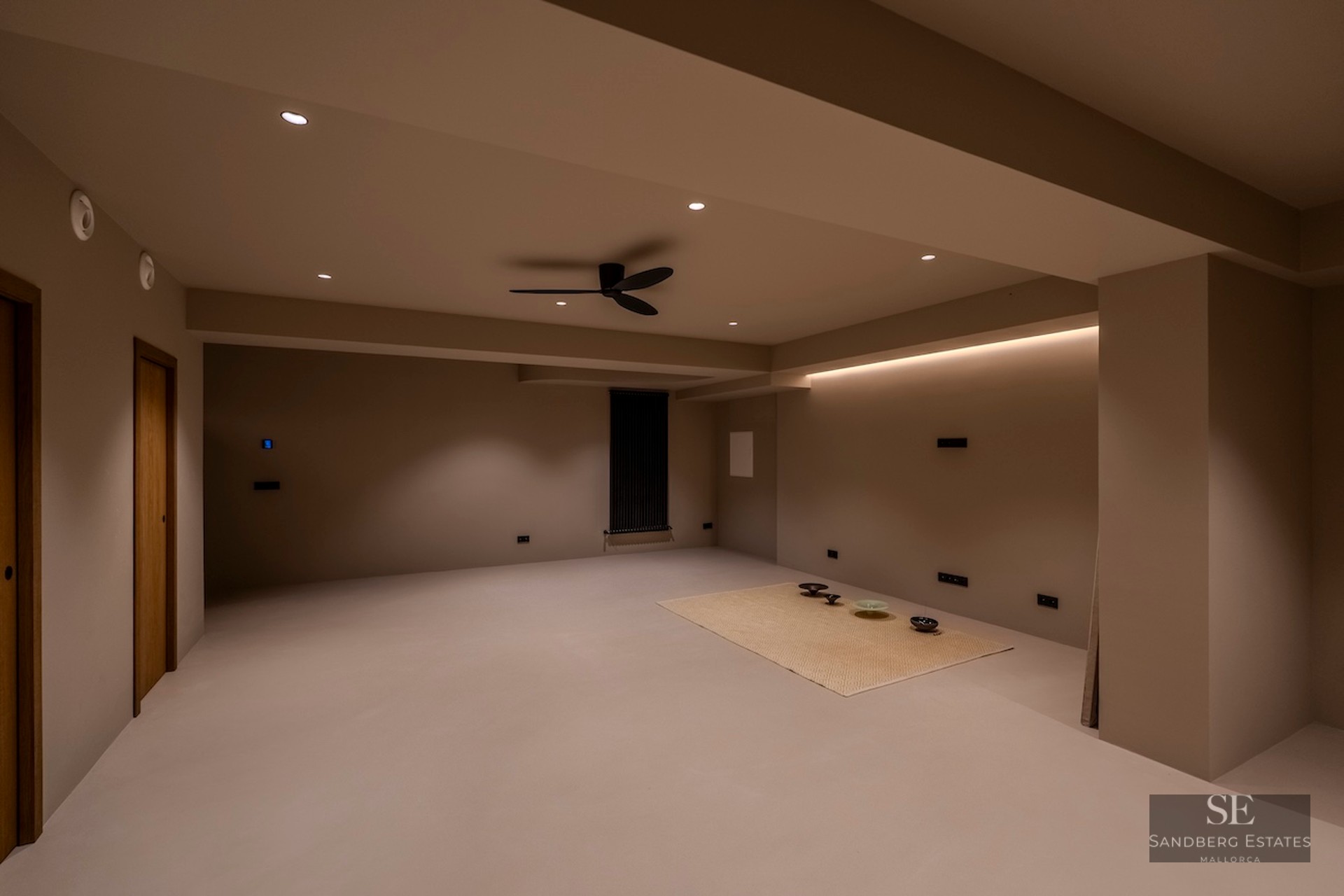 Pièce minimaliste vide avec murs beiges, éclairage LED indirect et ventilateur de plafond noir moderne.