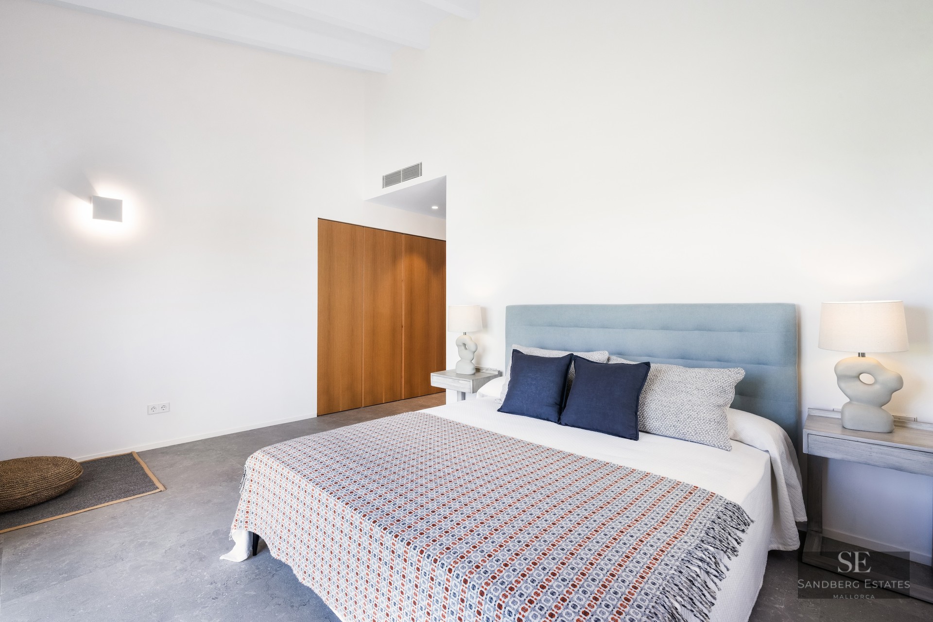 Bright bedroom with a large bed, light blue headboard, designer lamps, and built-in wooden wardrobe.