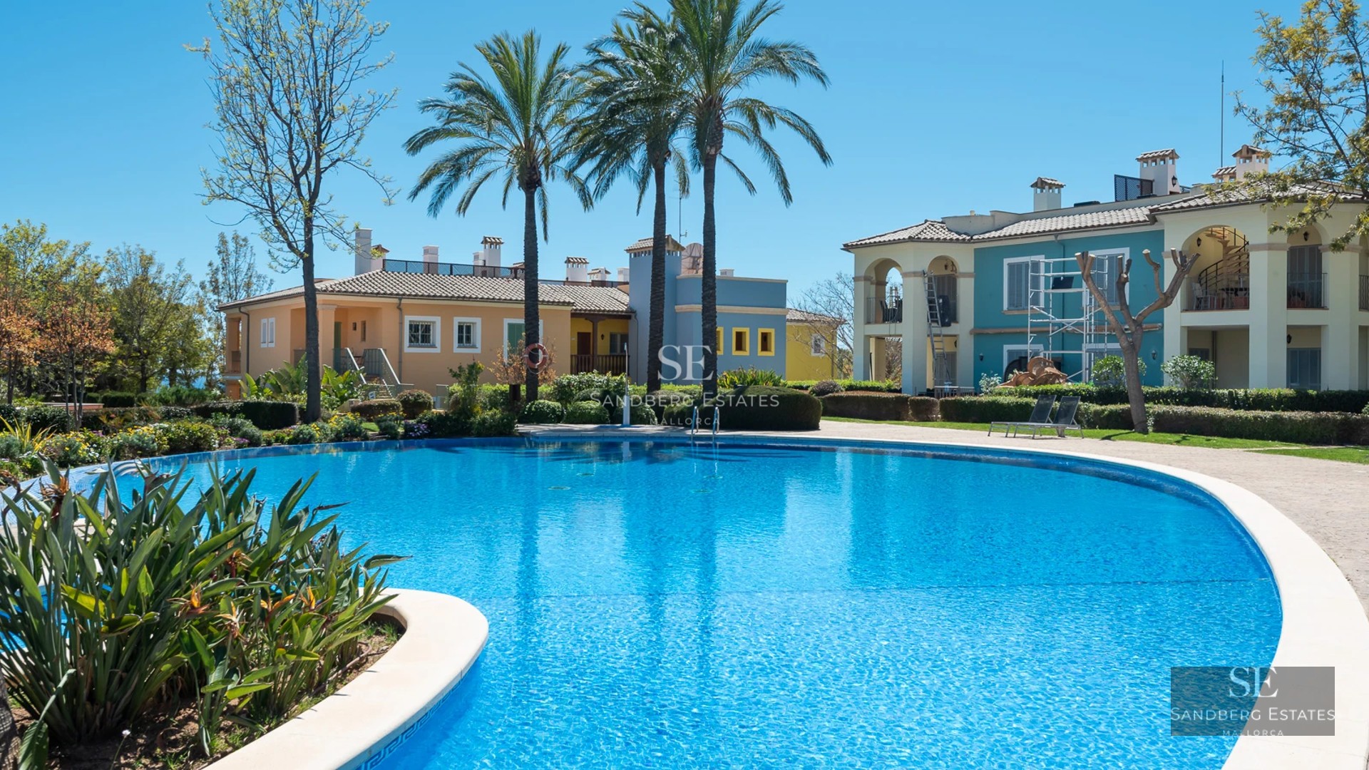 Image of a luxurious villa with infinity pool, manicured lawn, and modern architecture. Clear sky in the background.