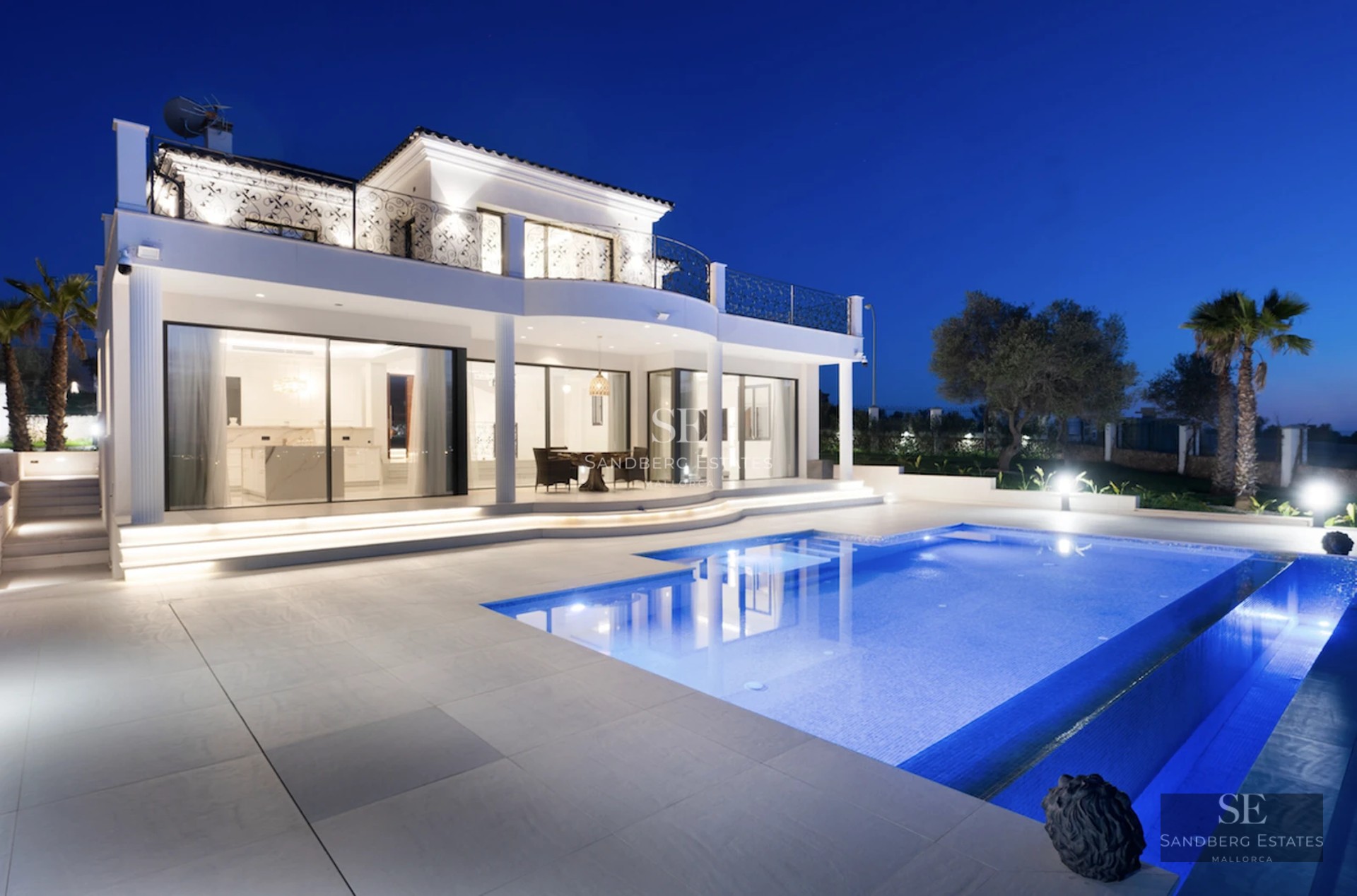 View of reflective infinity pool, modern architecture, large windows, and lush vegetation. Soft ambient lighting.