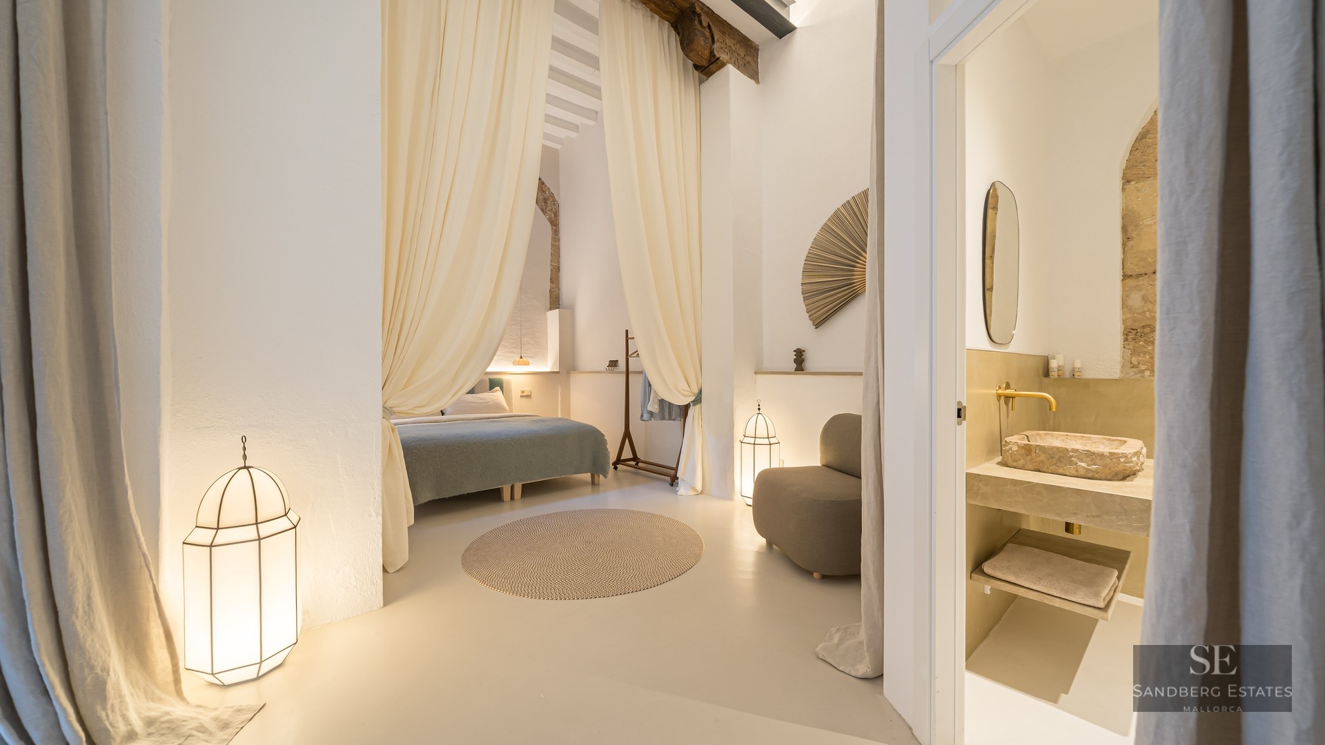 Elegant bedroom with high ceilings, flowing drapes, and a view into an ensuite bathroom with a rustic stone vessel sink.