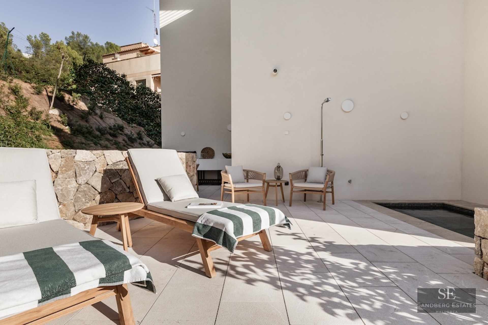 Modern outdoor terrace featuring wooden sunbeds, a small plunge pool, and a natural stone wall in bright sunlight.