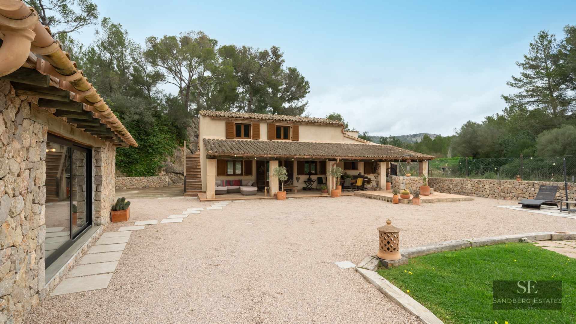 Exterior of a traditional stone house with terracotta tiles, wooden shutters, and a large gravel courtyard.