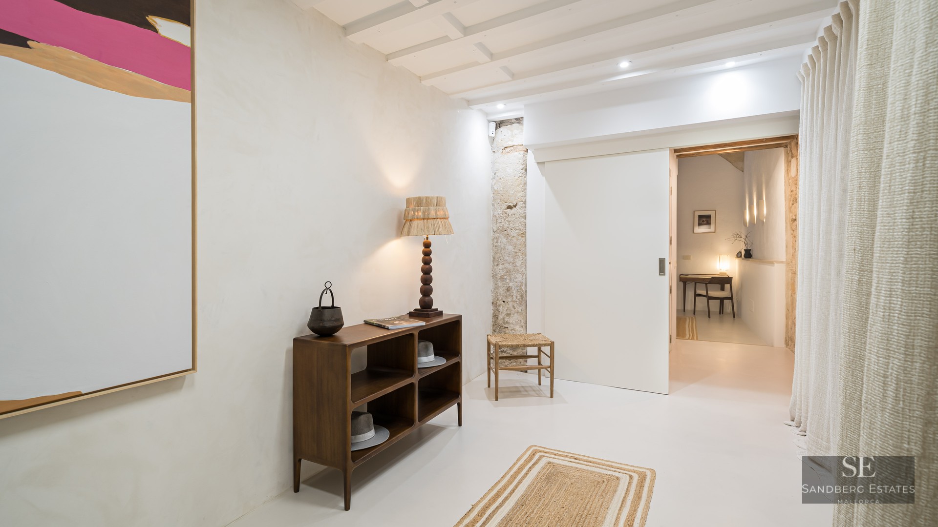 Modern hallway featuring a dark wood console table, exposed stone pillar, abstract art, and a white sliding door.