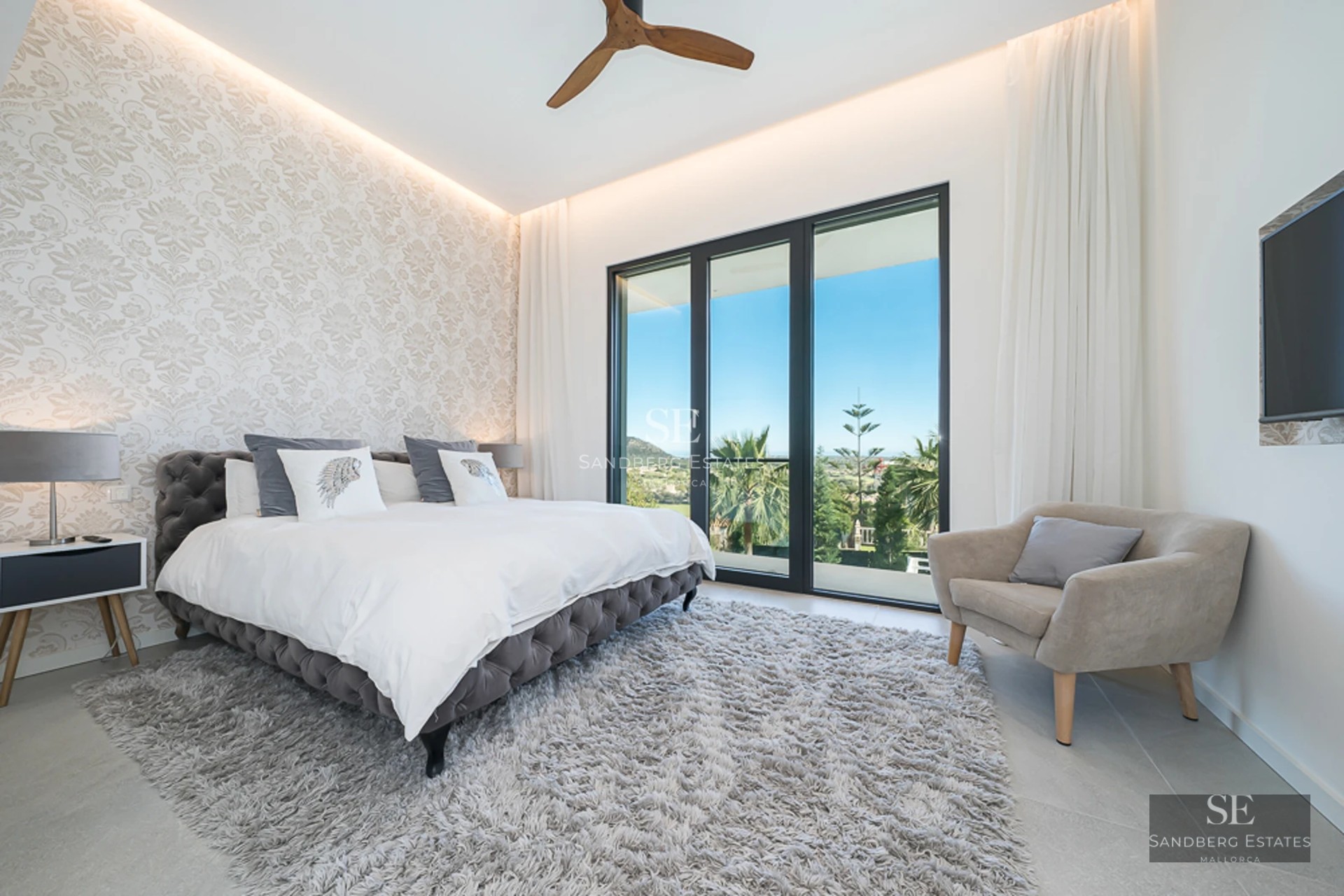 Panoramic view from a balcony with glass railing overlooking the sea. Modern and bright interior. Potted plants.