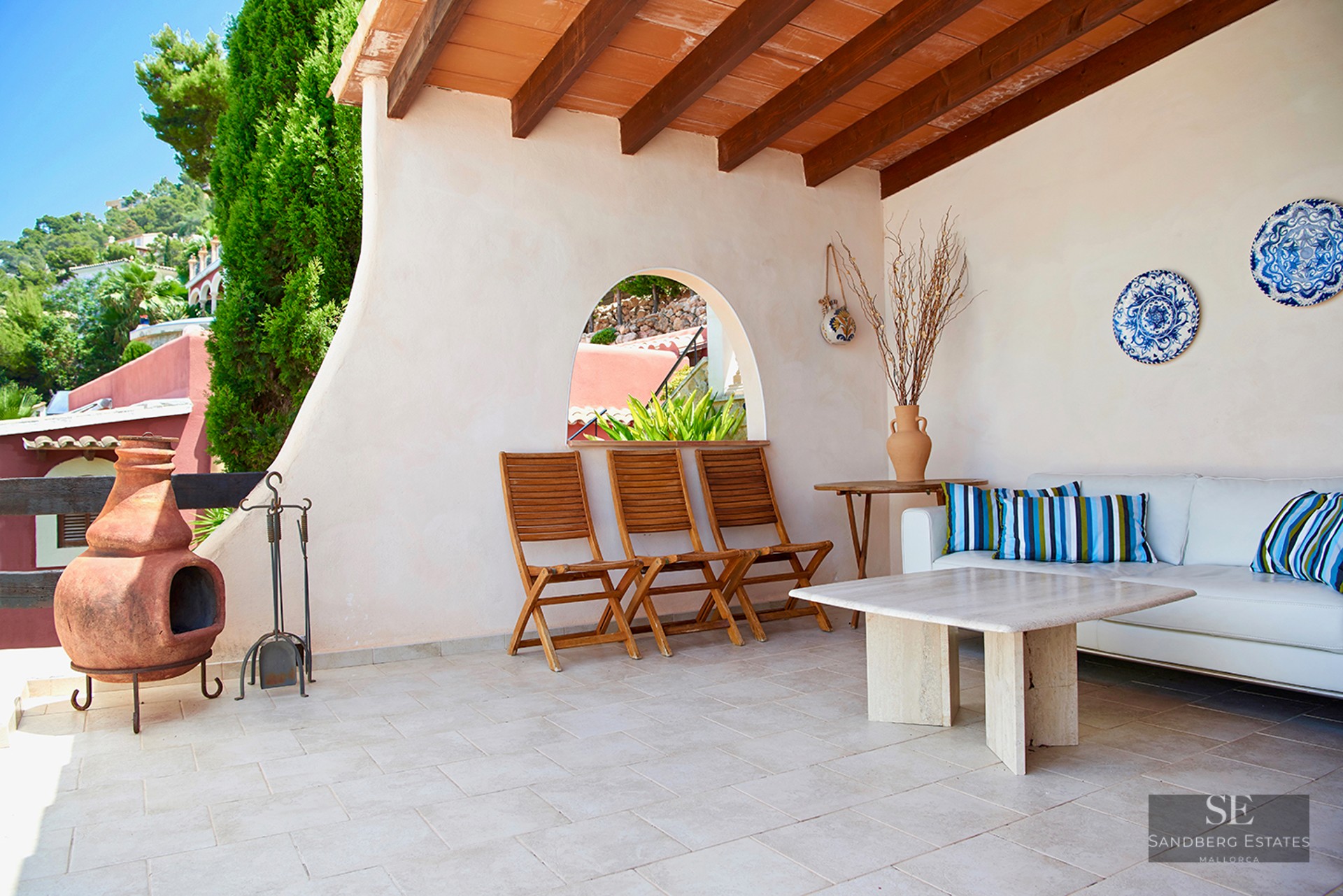 Covered terrace featuring white sofas, marble table, terracotta fireplace, and exposed wooden beams.