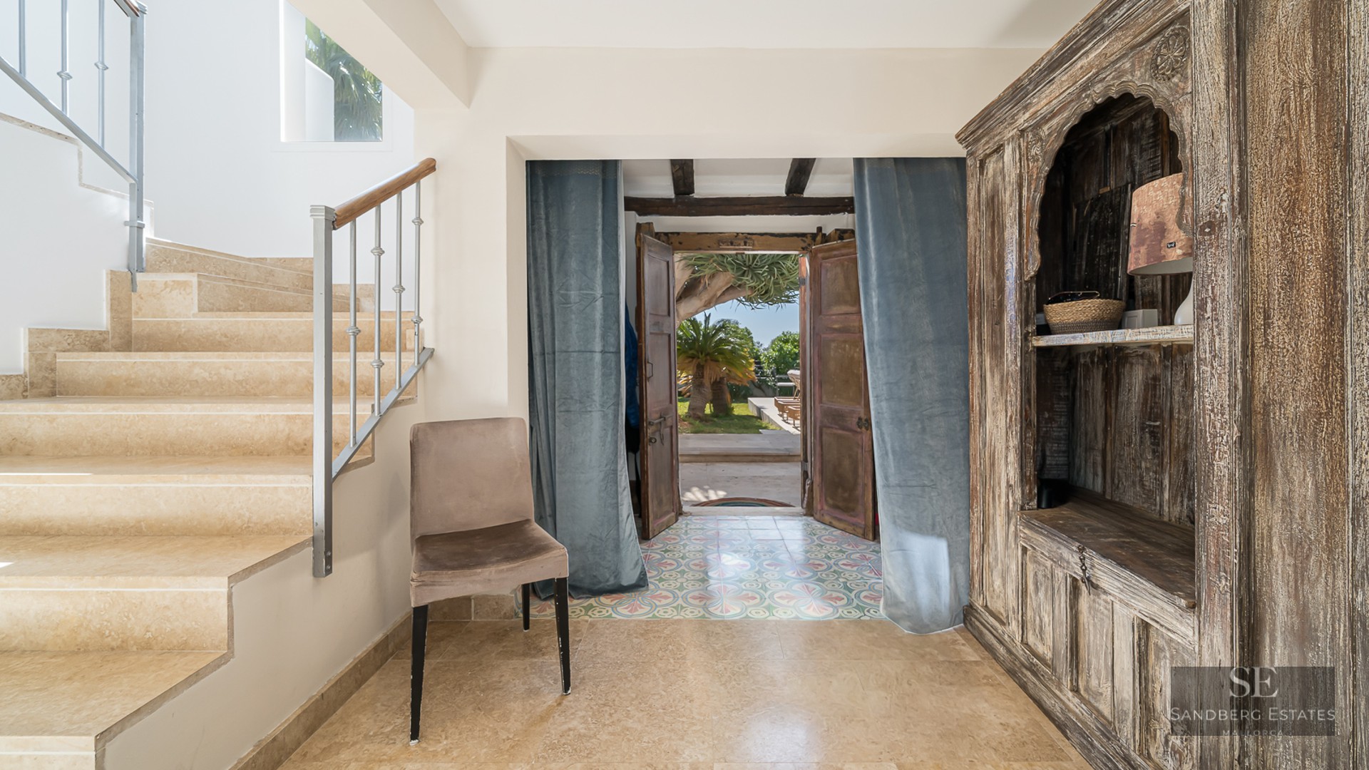 Entrance hall featuring a stone staircase, large antique wooden cabinet, and open doors leading to a sunny garden.