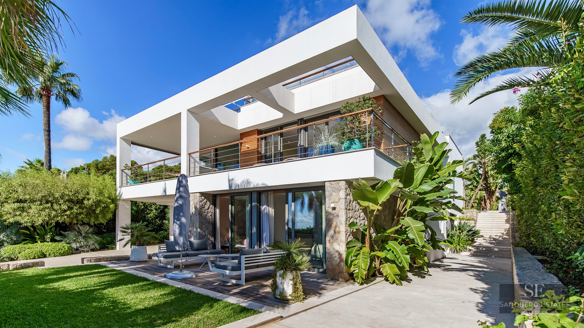 Villa moderne blanche sur deux niveaux avec pierre naturelle et jardin tropical sous un ciel bleu.