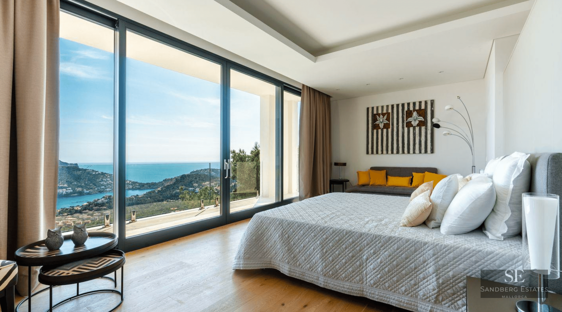 Modern master bedroom featuring floor-to-ceiling glass doors with a stunning view of the sea and coastline.