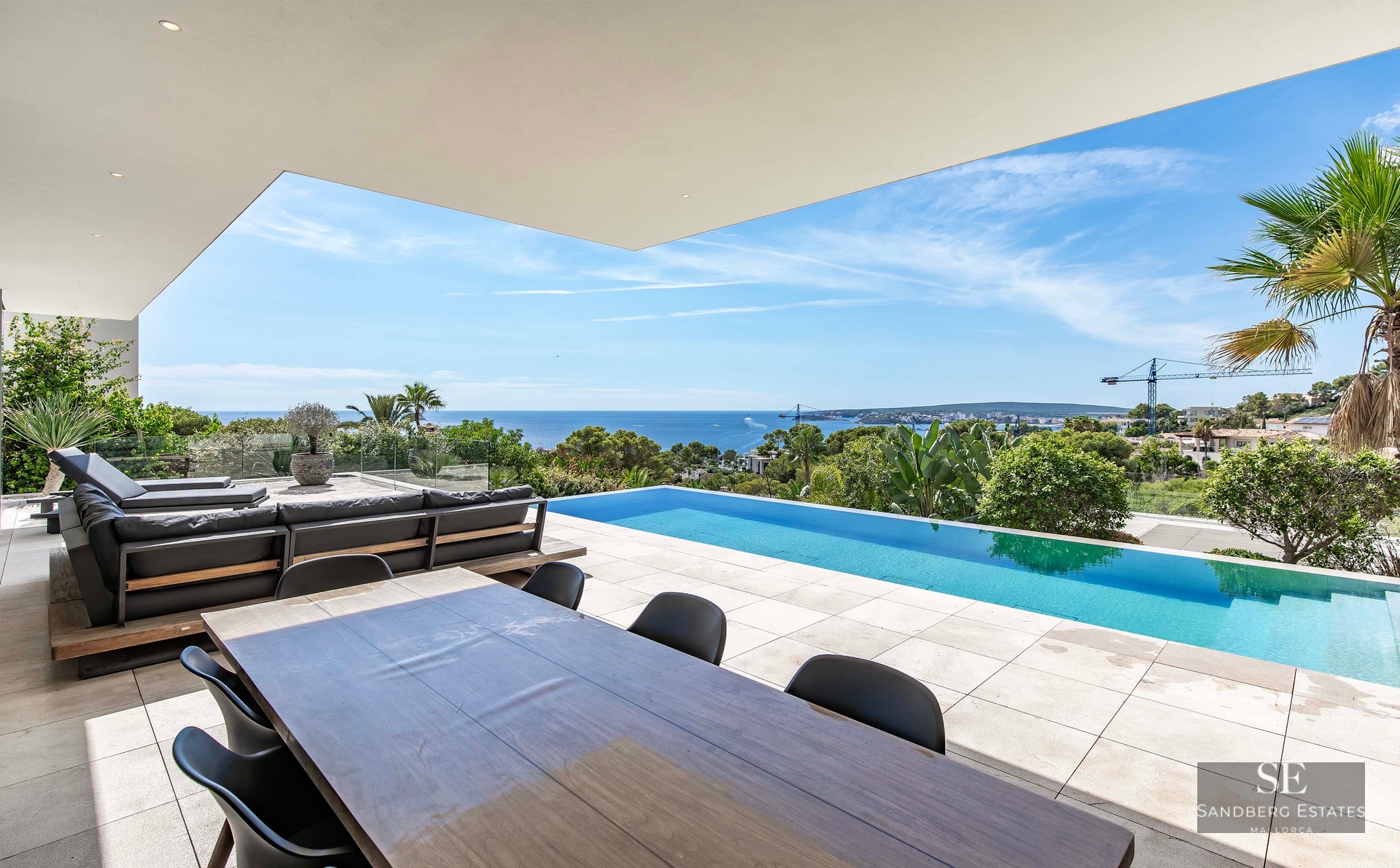 A modern luxury terrace featuring an infinity pool overlooking the ocean, with outdoor dining and lounge seating.