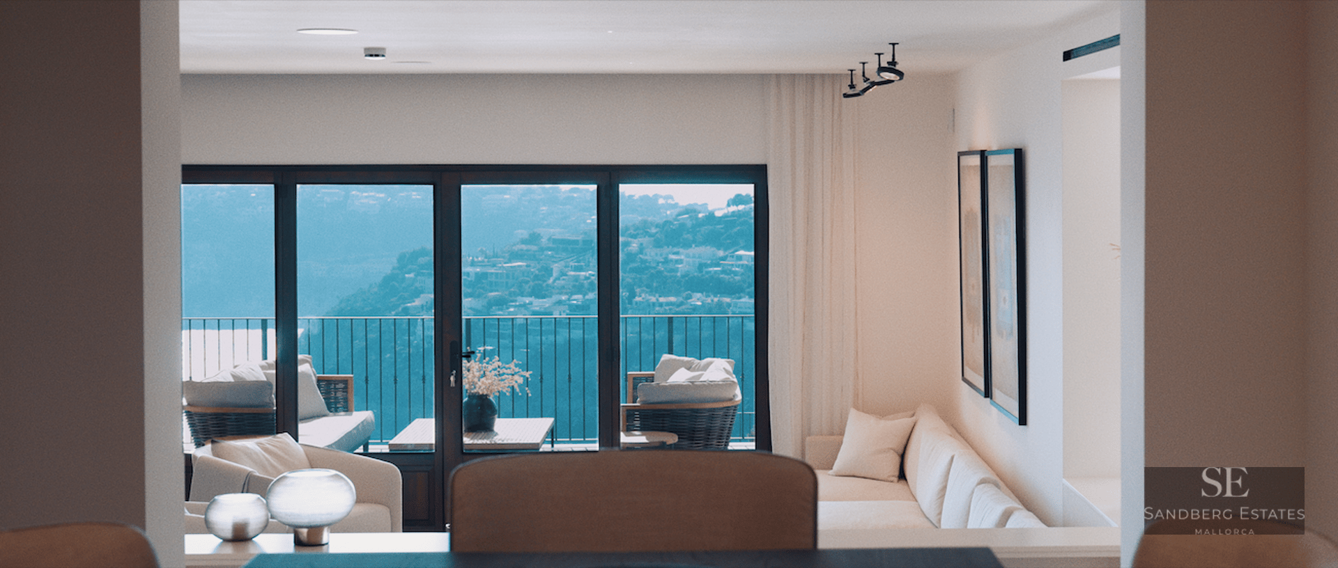 Bright living room with white sofa and large windows overlooking a scenic hillside and balcony furniture.