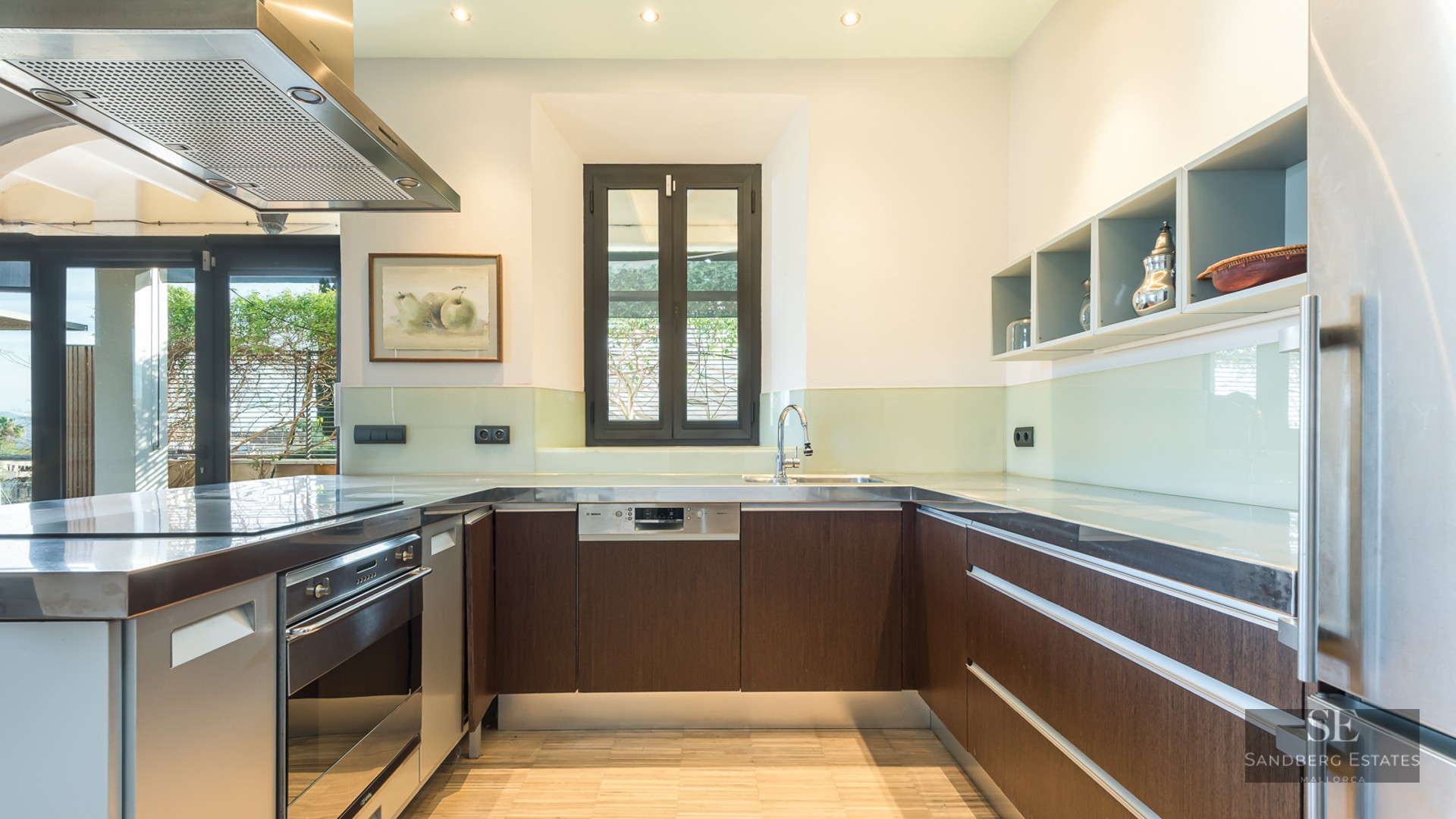 Modern kitchen with dark wood cabinets, stainless steel countertops, and a glass backsplash under bright lighting.