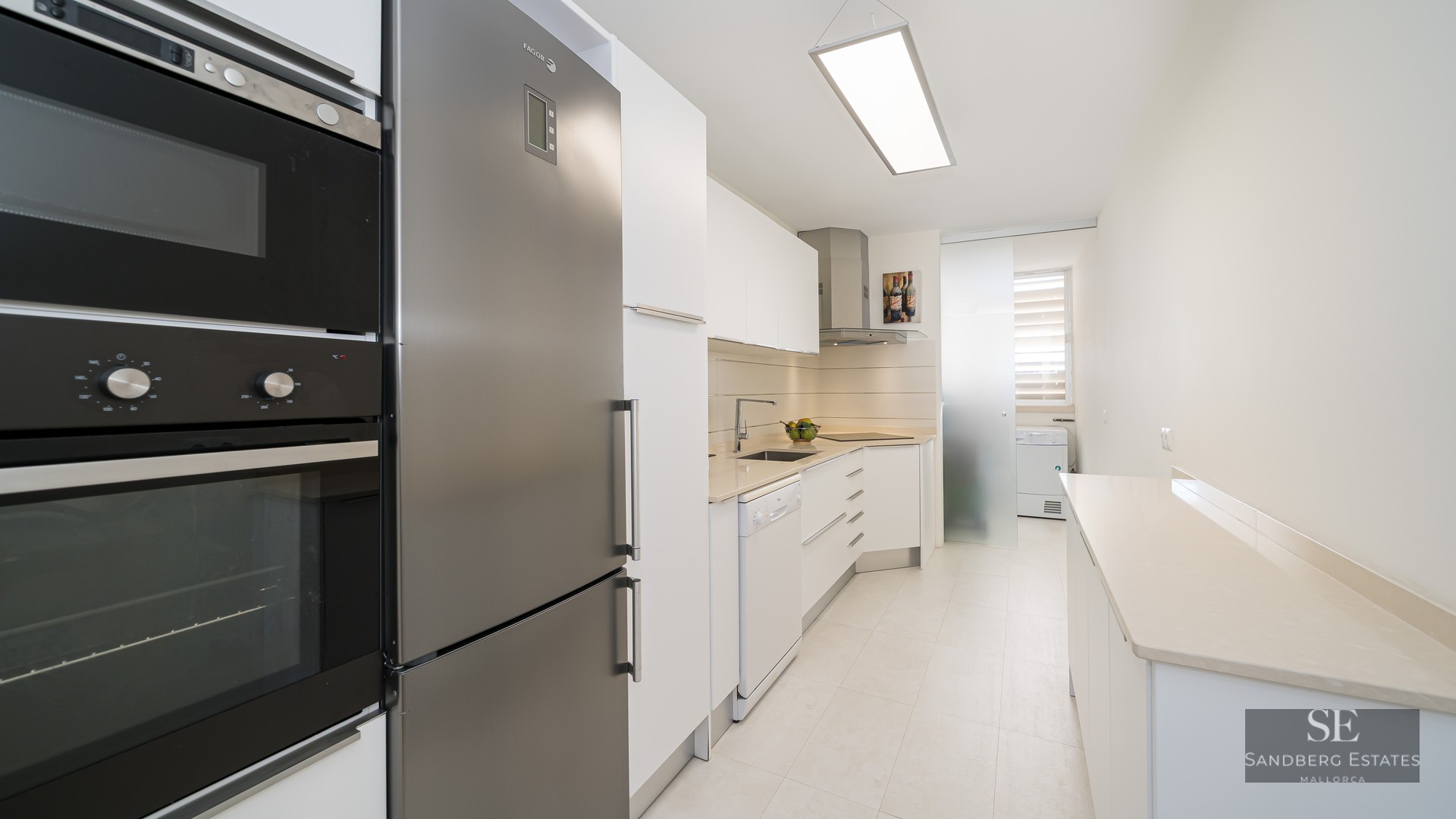 A modern galley-style kitchen with white cabinetry and stainless steel appliances.