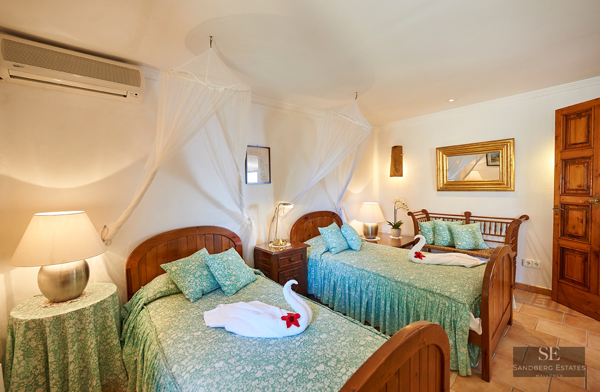 Two wooden twin beds with green floral bedding and white mosquito nets in a rustic room with terracotta floors.
