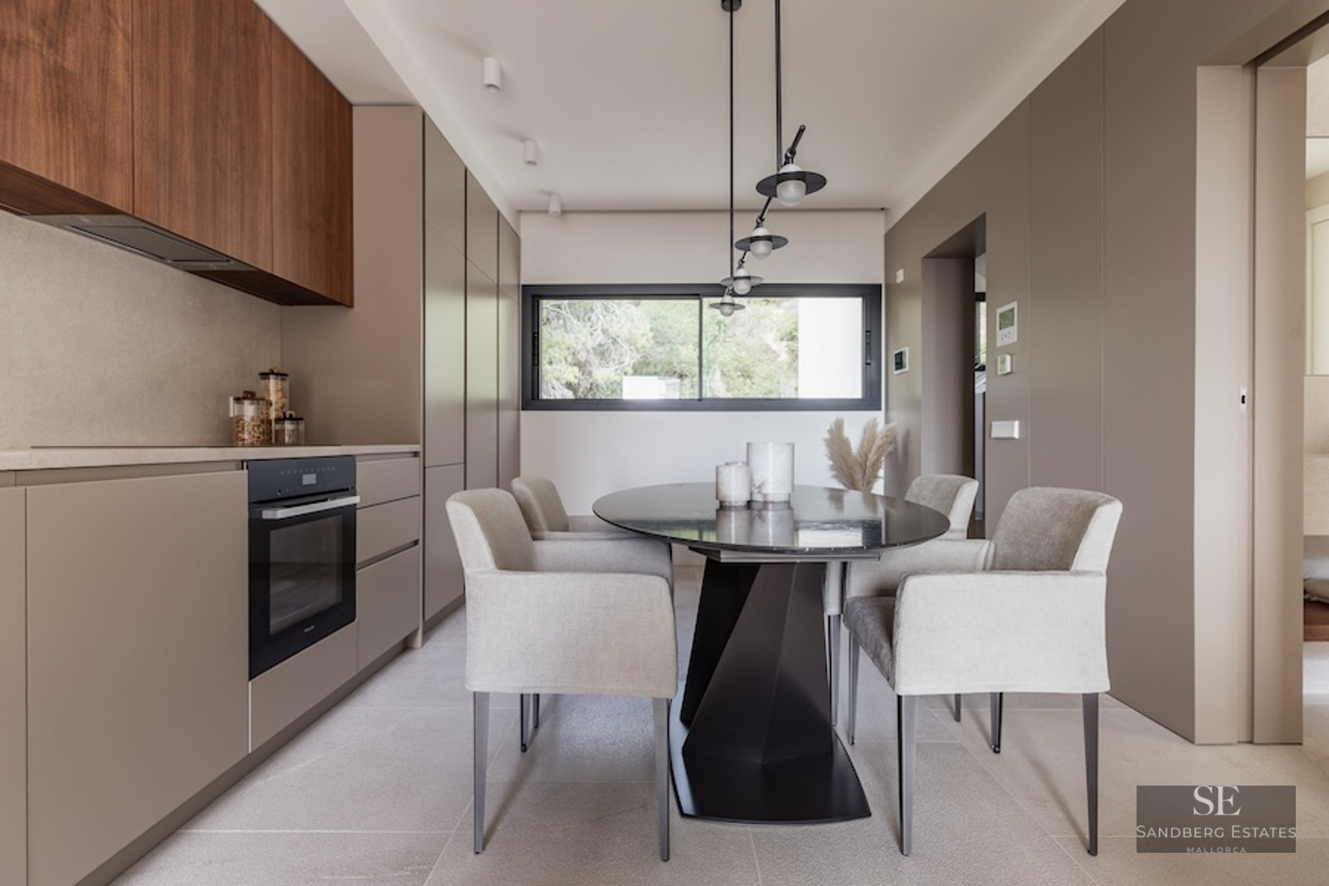 Modern dining room with oval black table, grey armchairs, and taupe cabinetry under designer pendant lights.