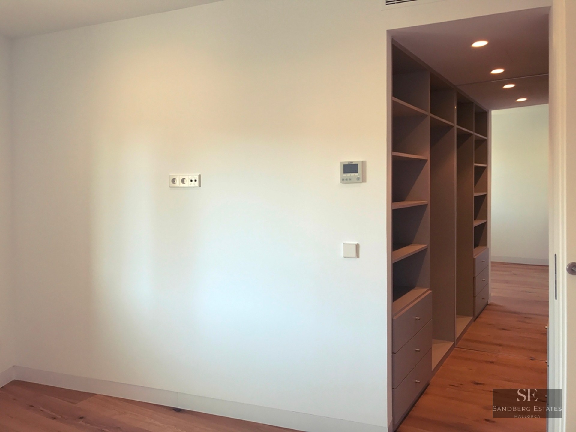 White room with light wood floors and a grey built-in shelving and drawer unit leading into a hallway.