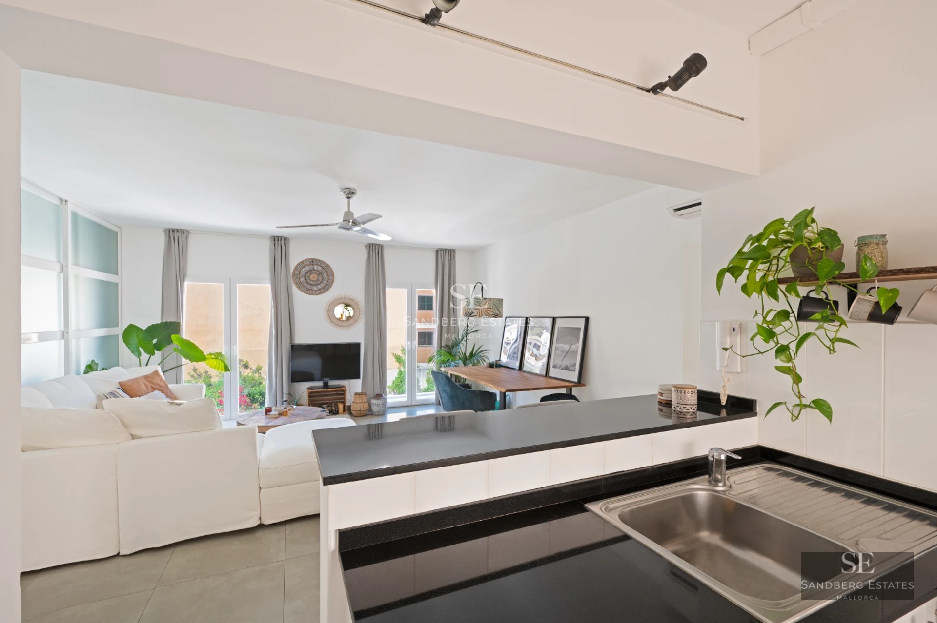 Spacious balcony overlooking the sea. Wooden floors, glass railing, modern outdoor furniture. Clear blue sky.