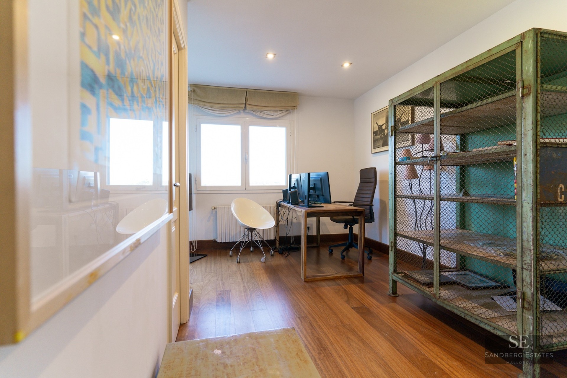 Home office with wood floors, desk with dual monitors, and a vintage green metal mesh cabinet.