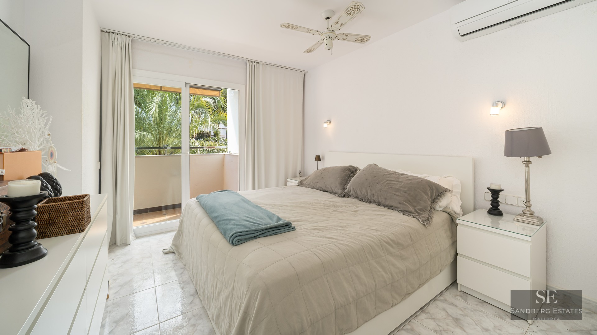 Bright bedroom with double bed, marble floors, and balcony doors showing palm trees.